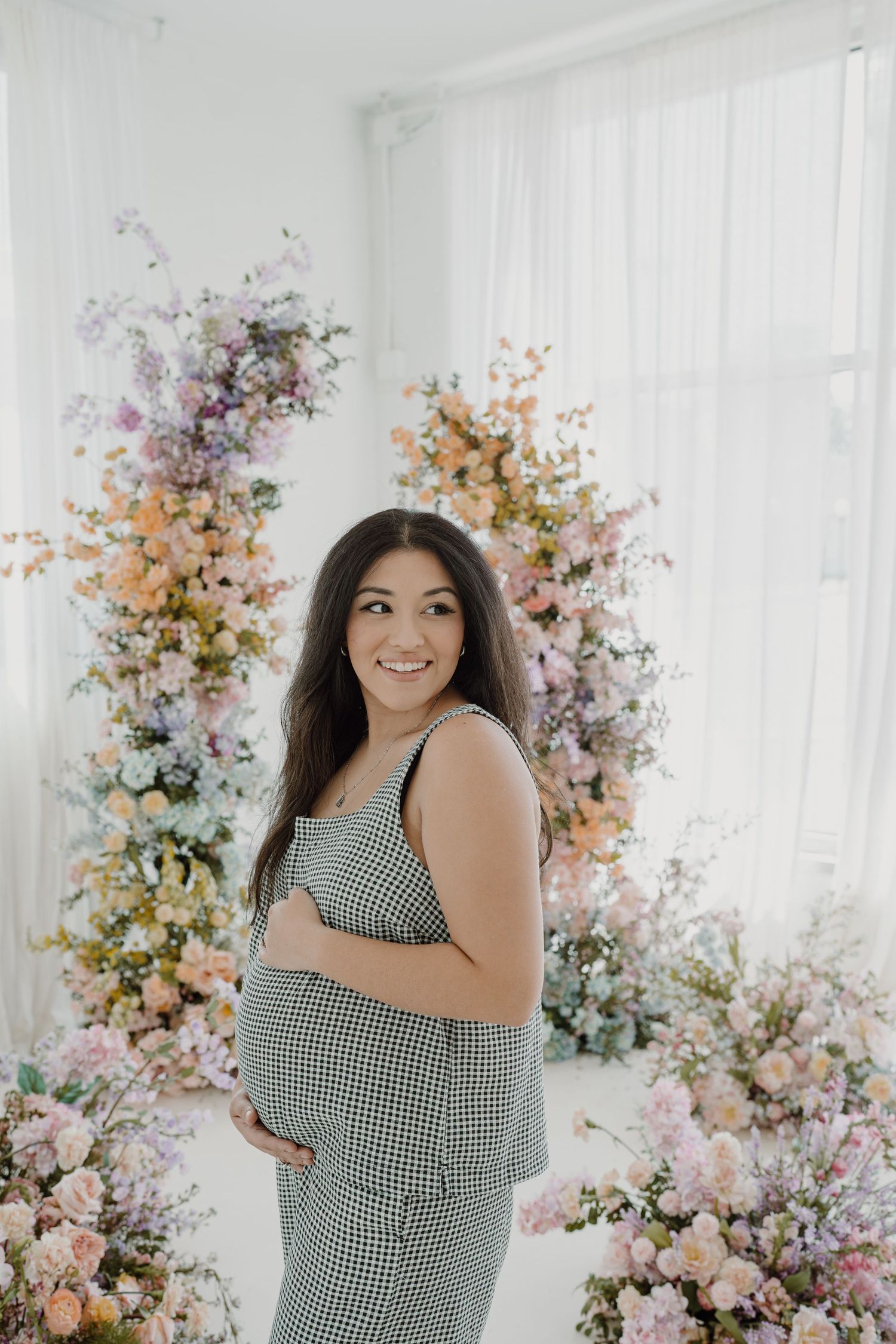 Elegant maternity photos captured in a bright studio with pastel floral installations.