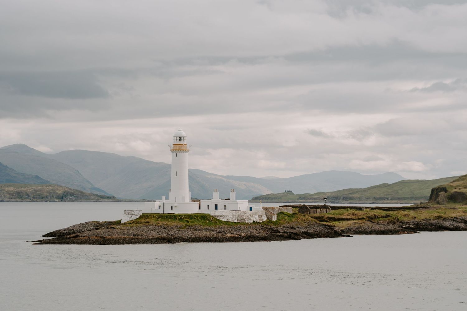 White lighthouse standing on a rocky peninsula against dramatic cloudy skies.