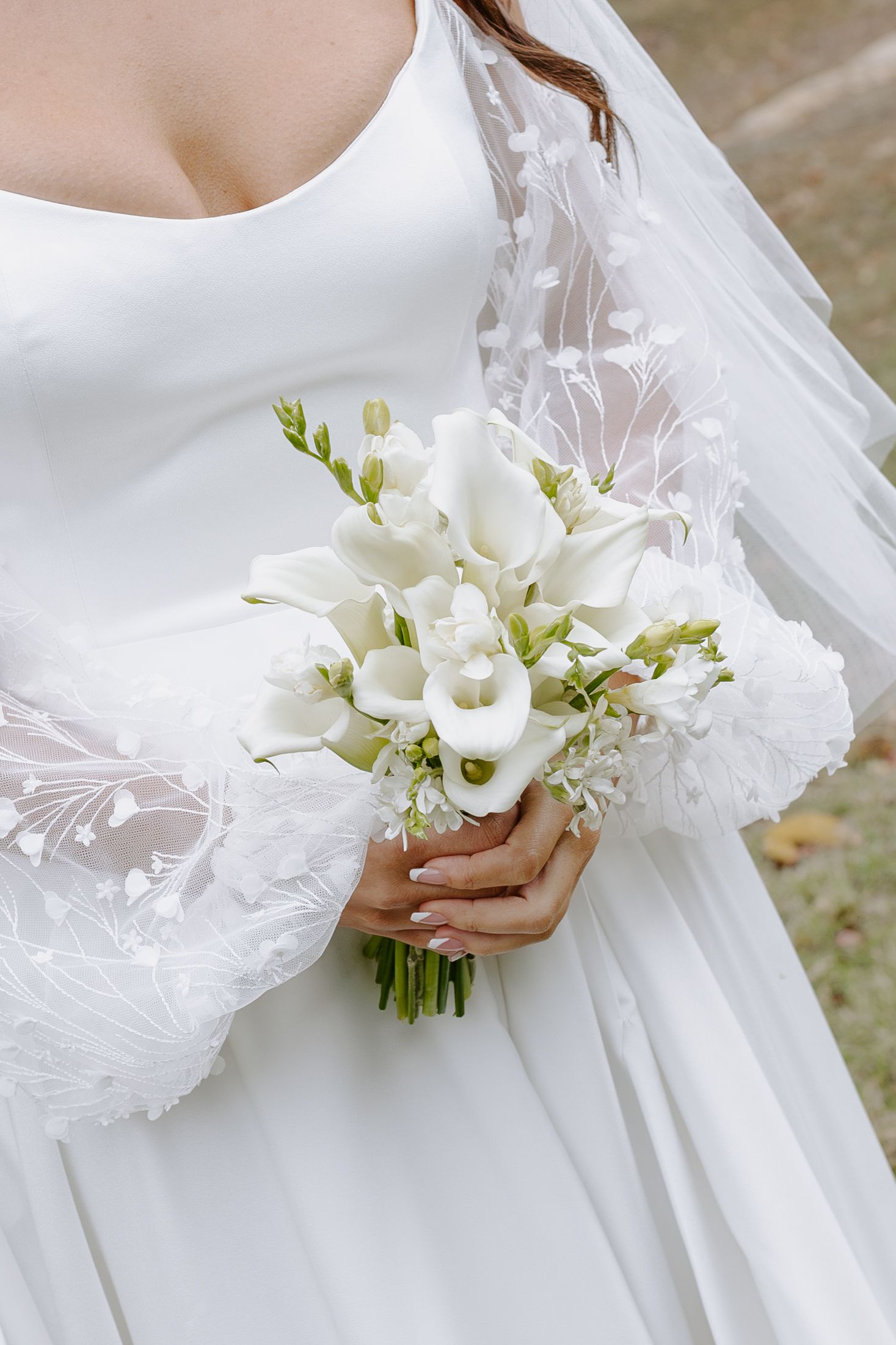 A close-up of a white calla lily wedding bouquet held against a lace-detailed wedding dress.
