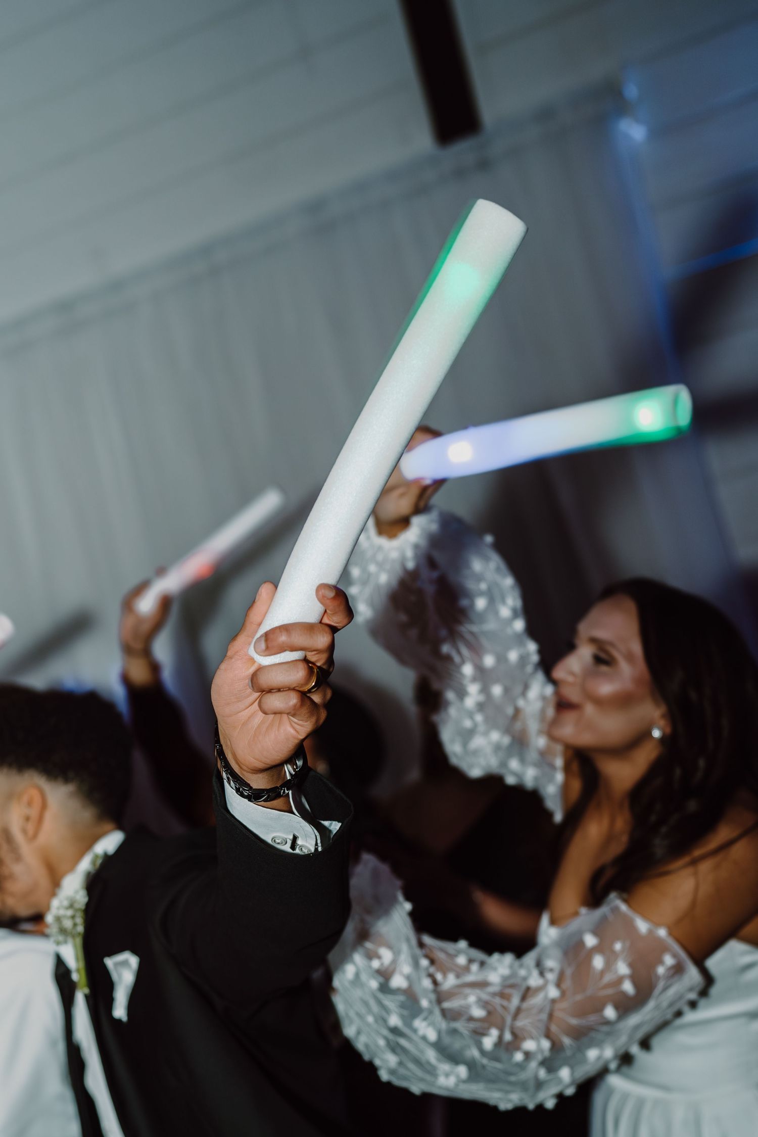 A guest raises a glowing LED foam stick while dancing at an elegant wedding reception.