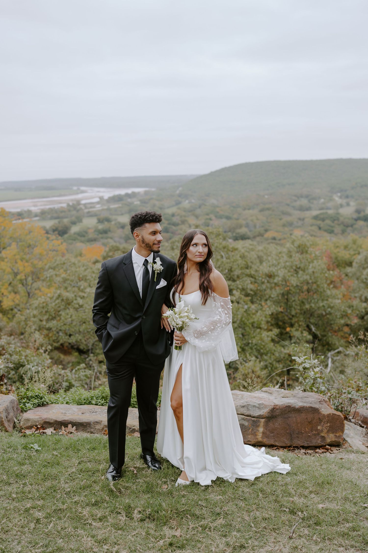 Couple poses for romantic portraits on hilltop with sweeping valley views.