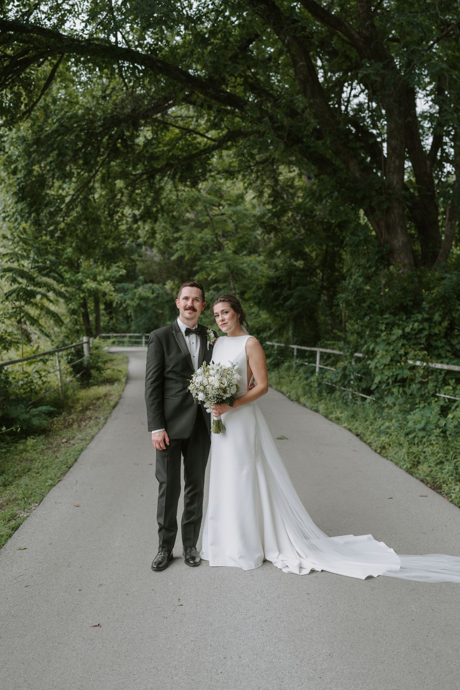 Wedding portrait featuring a couple standing together on a peaceful forest path with natural lighting.