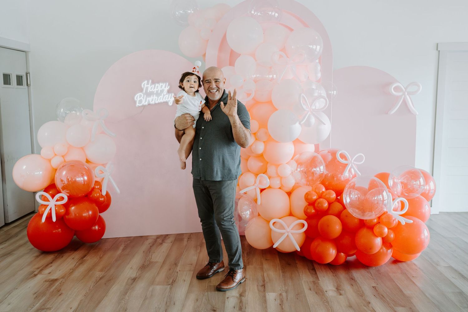 Festive balloon display with ombre effect from light pink to coral red against white wall.