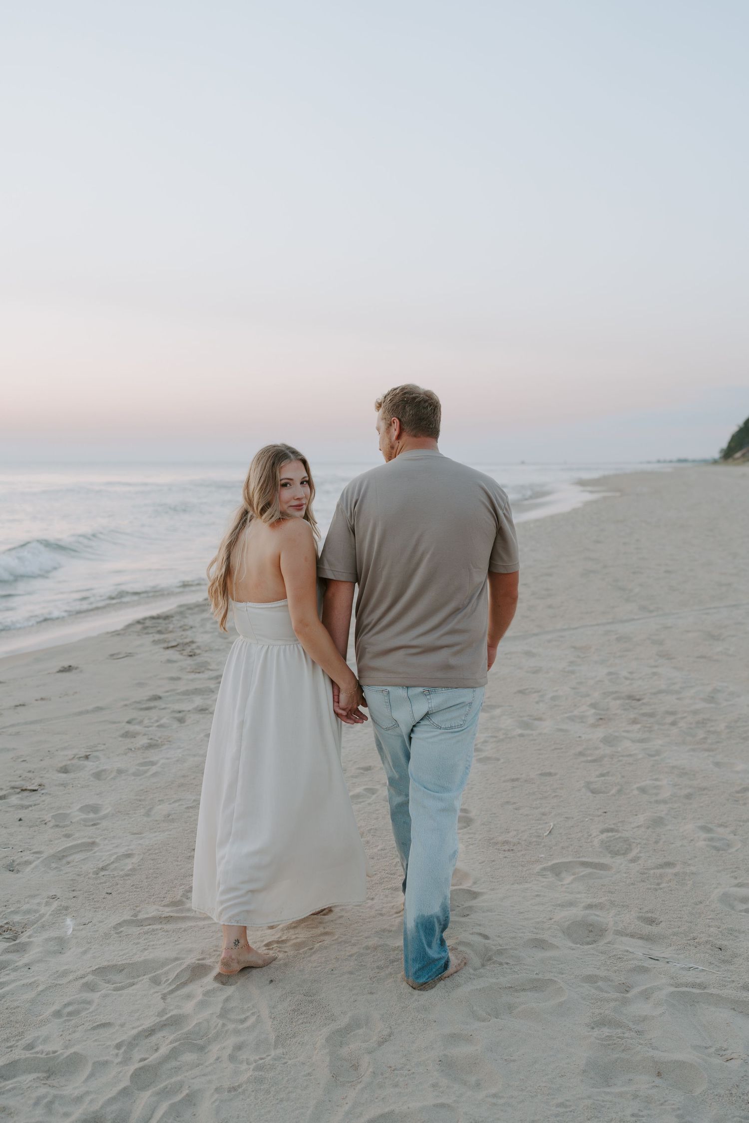 A couple walks barefoot in the sand during a peaceful beach sunset.
