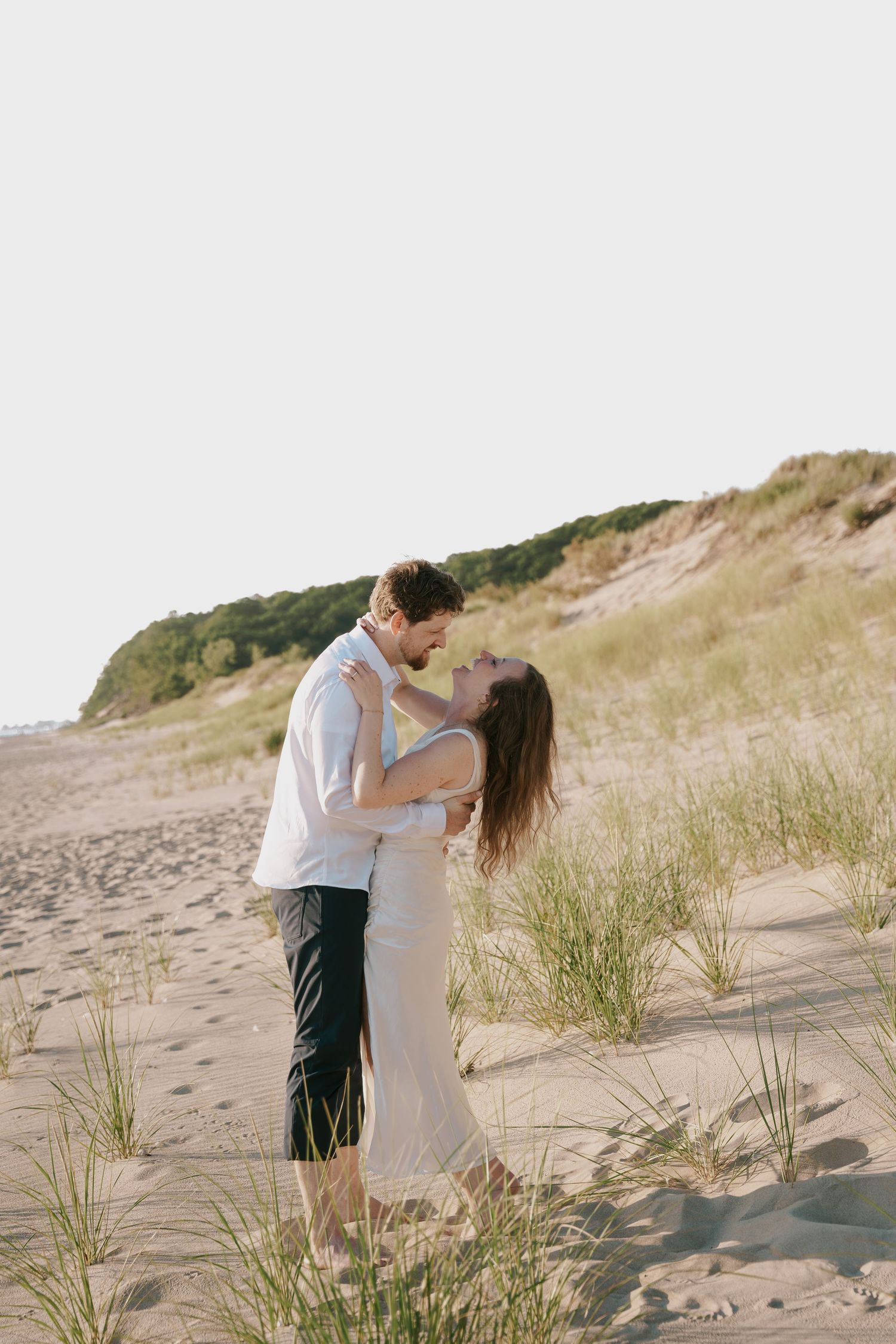 A tender embrace between a couple standing among beach grass with coastal cliffs in the background.