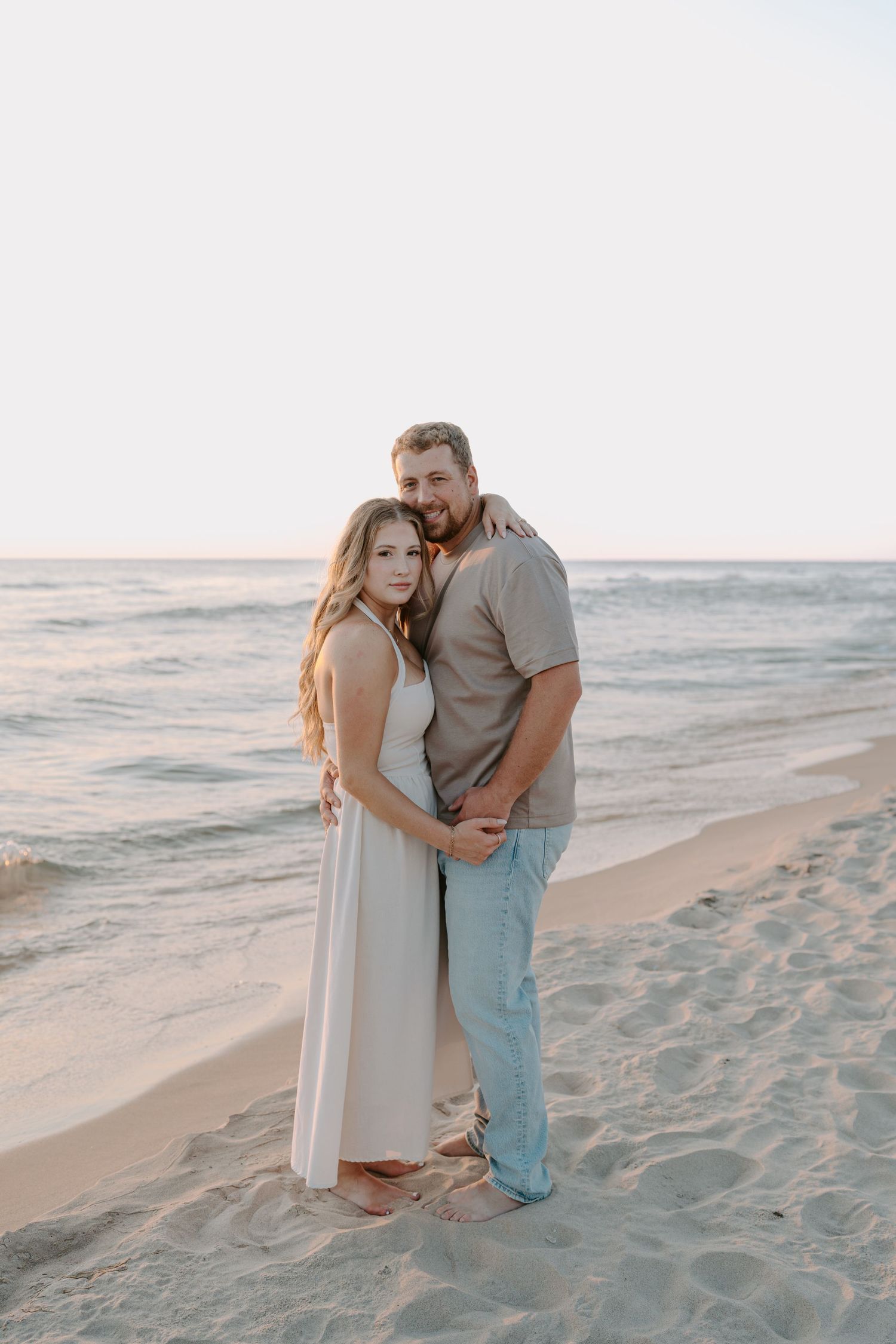 Couple embracing on beach with ocean waves in background during sunset.
