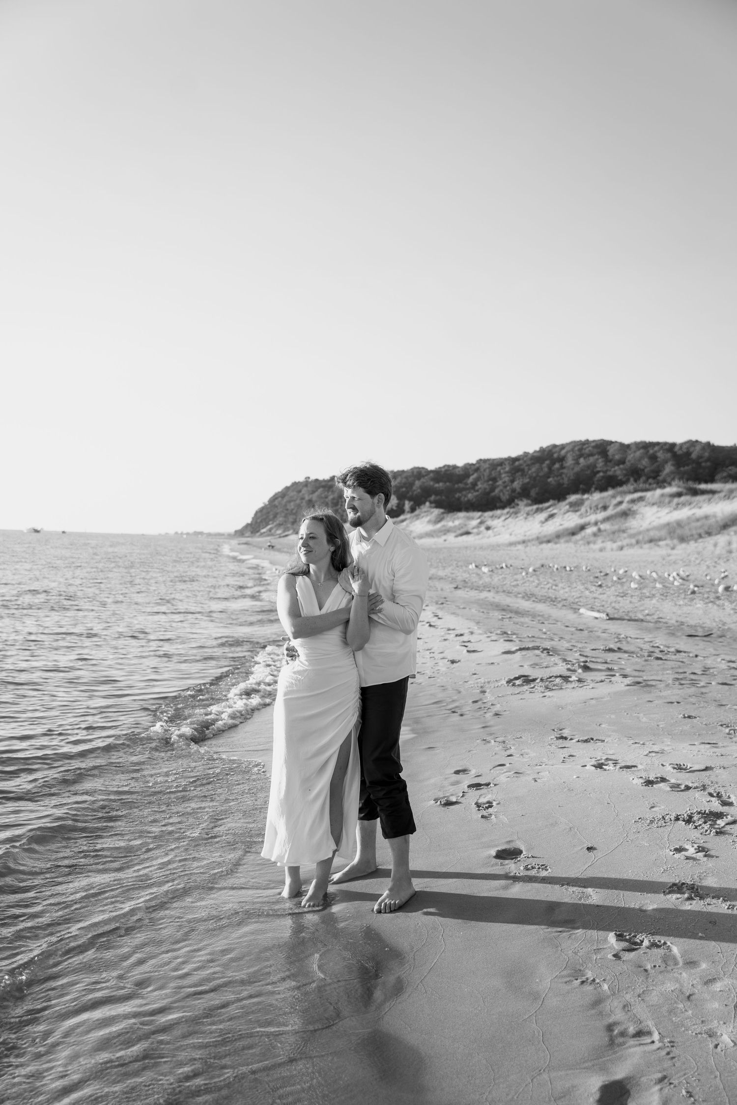 A black and white photo captures a couple embracing on a scenic beach.
