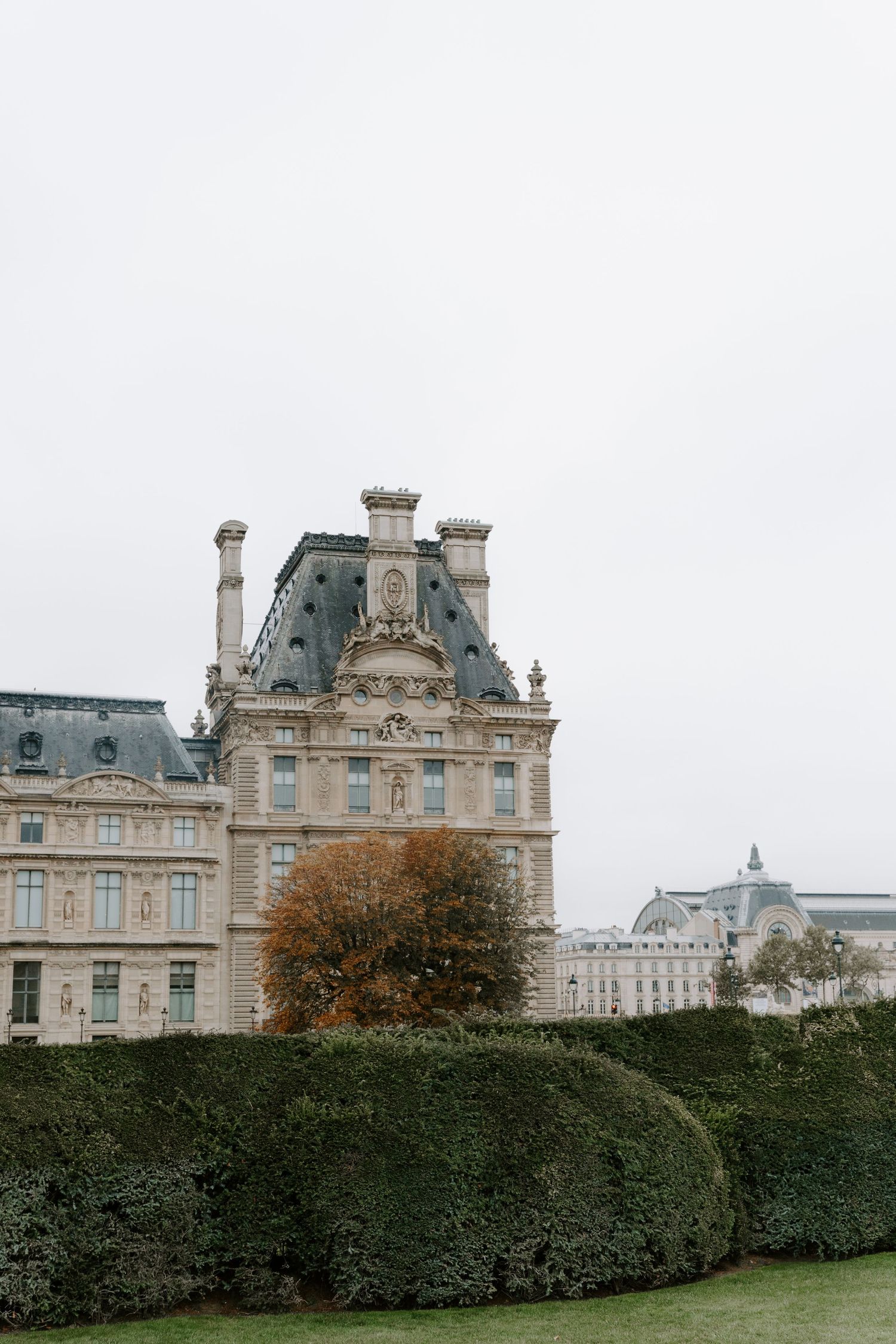 Elegant French architecture with manicured hedges at the Louvre Palace gardens.