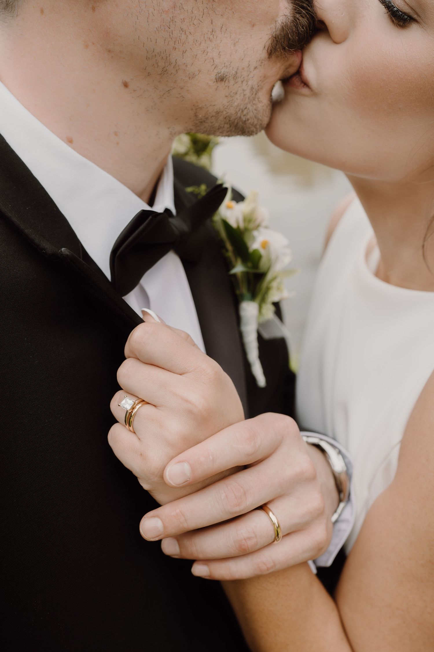 Intimate close-up of newlyweds sharing a tender moment showing wedding rings and formal attire.