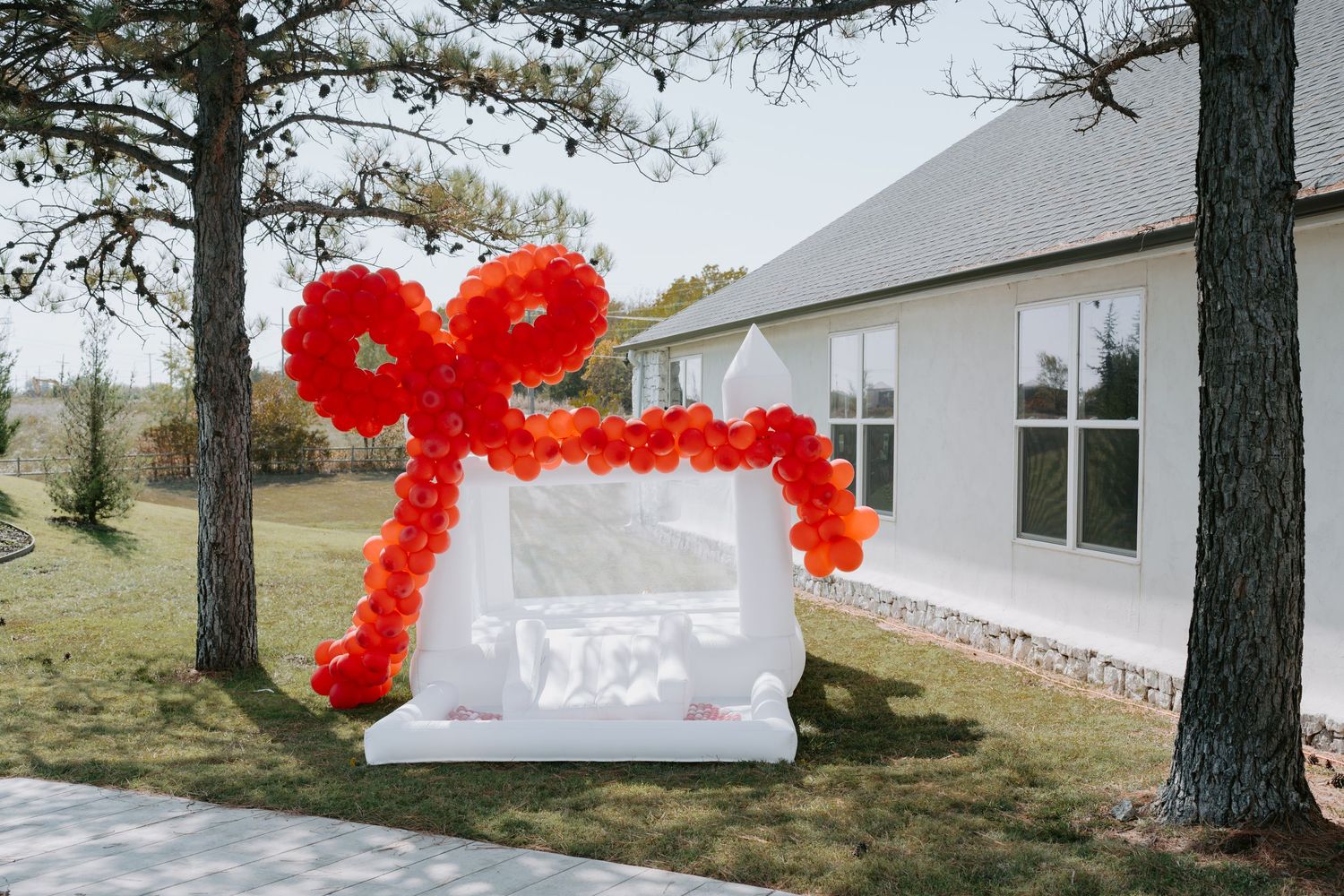 Red balloon arch installation outside a white building among pine trees.