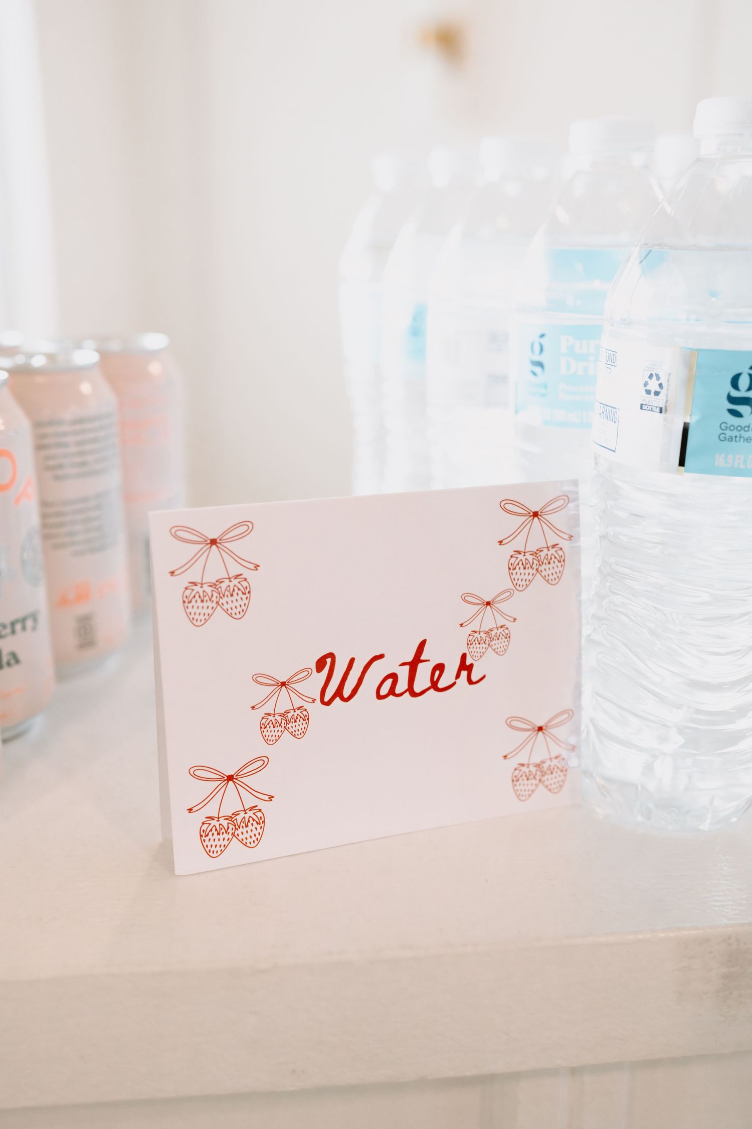 Row of pink water labels with strawberry bow designs on white bottles.