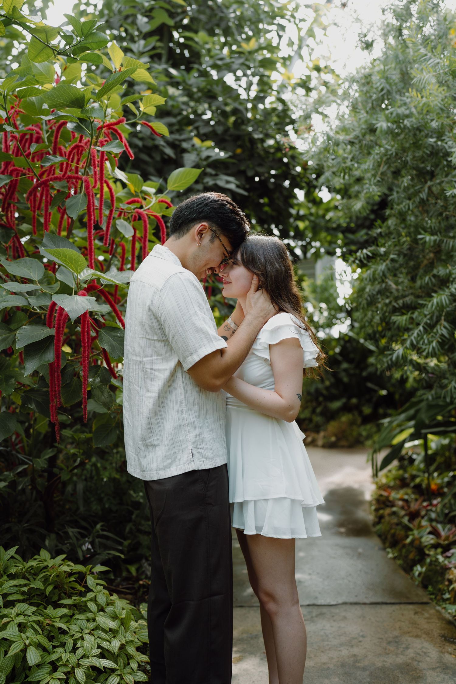 A romantic couple shares an intimate moment in a lush garden pathway surrounded by greenery.