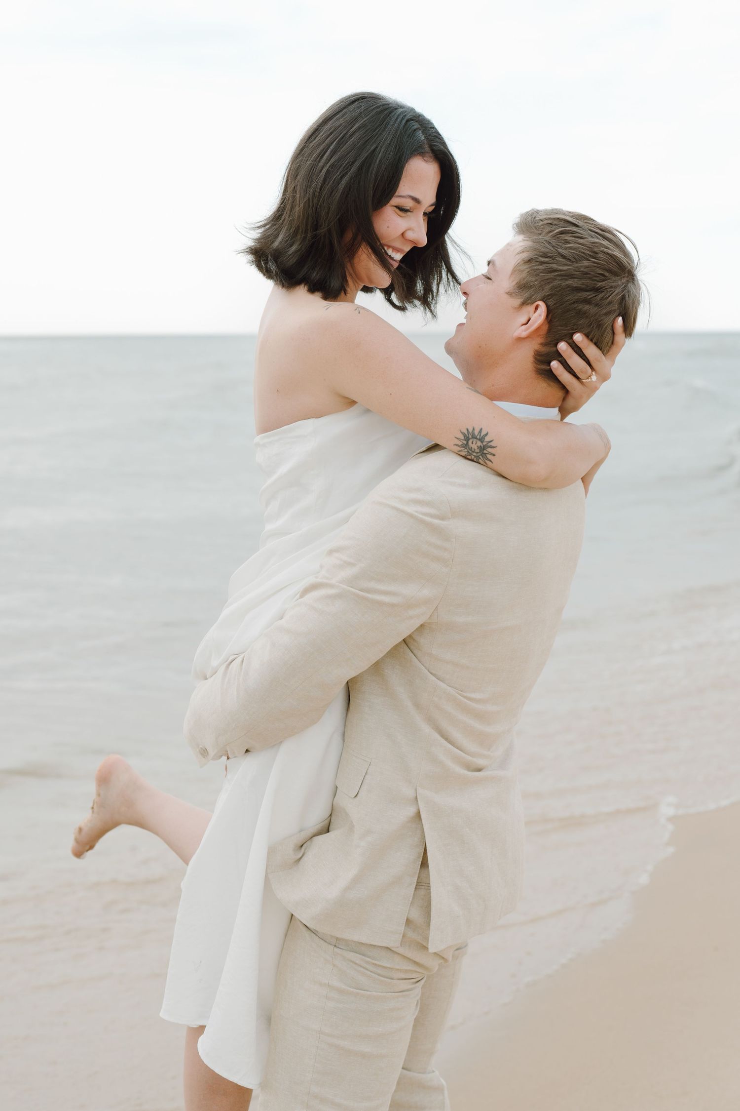 A couple shares an intimate moment while standing together on a peaceful beach shoreline.