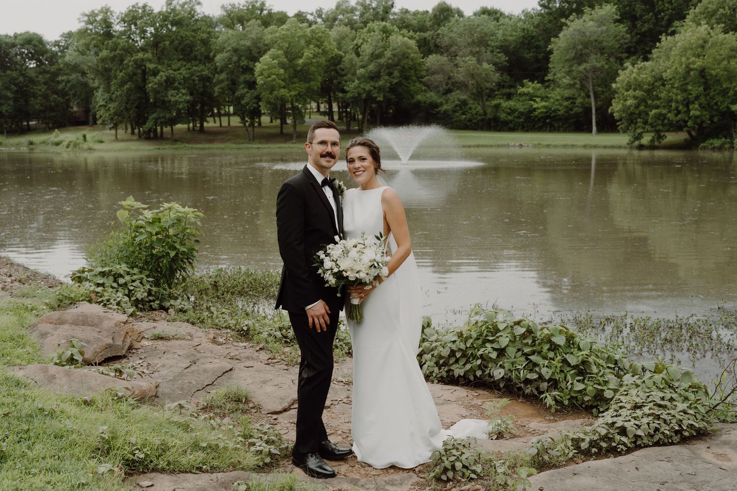 Romantic wedding portraits captured beside a tranquil pond with natural landscape elements.