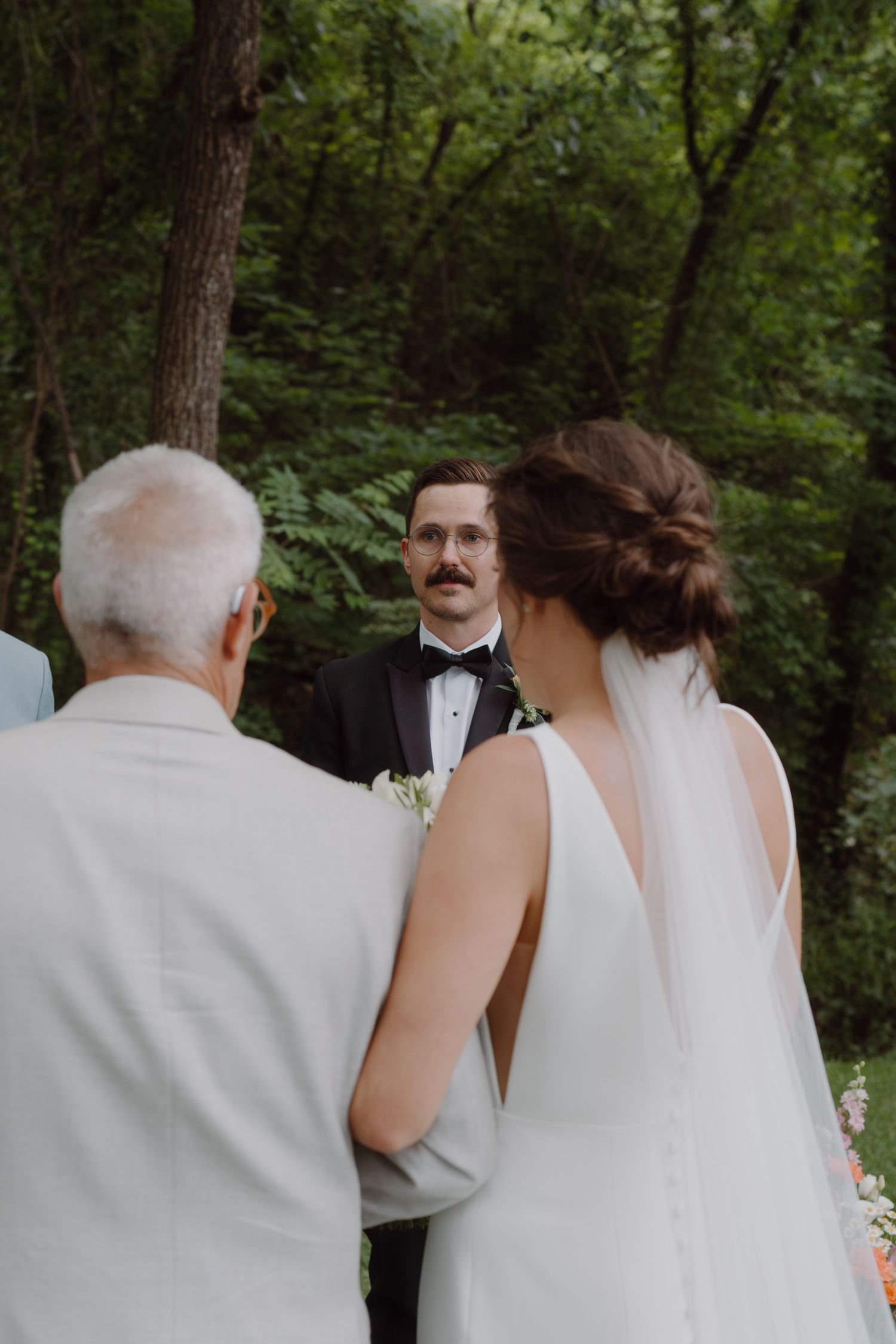 Wedding ceremony participants gather in a lush green forest setting with elegant attire.