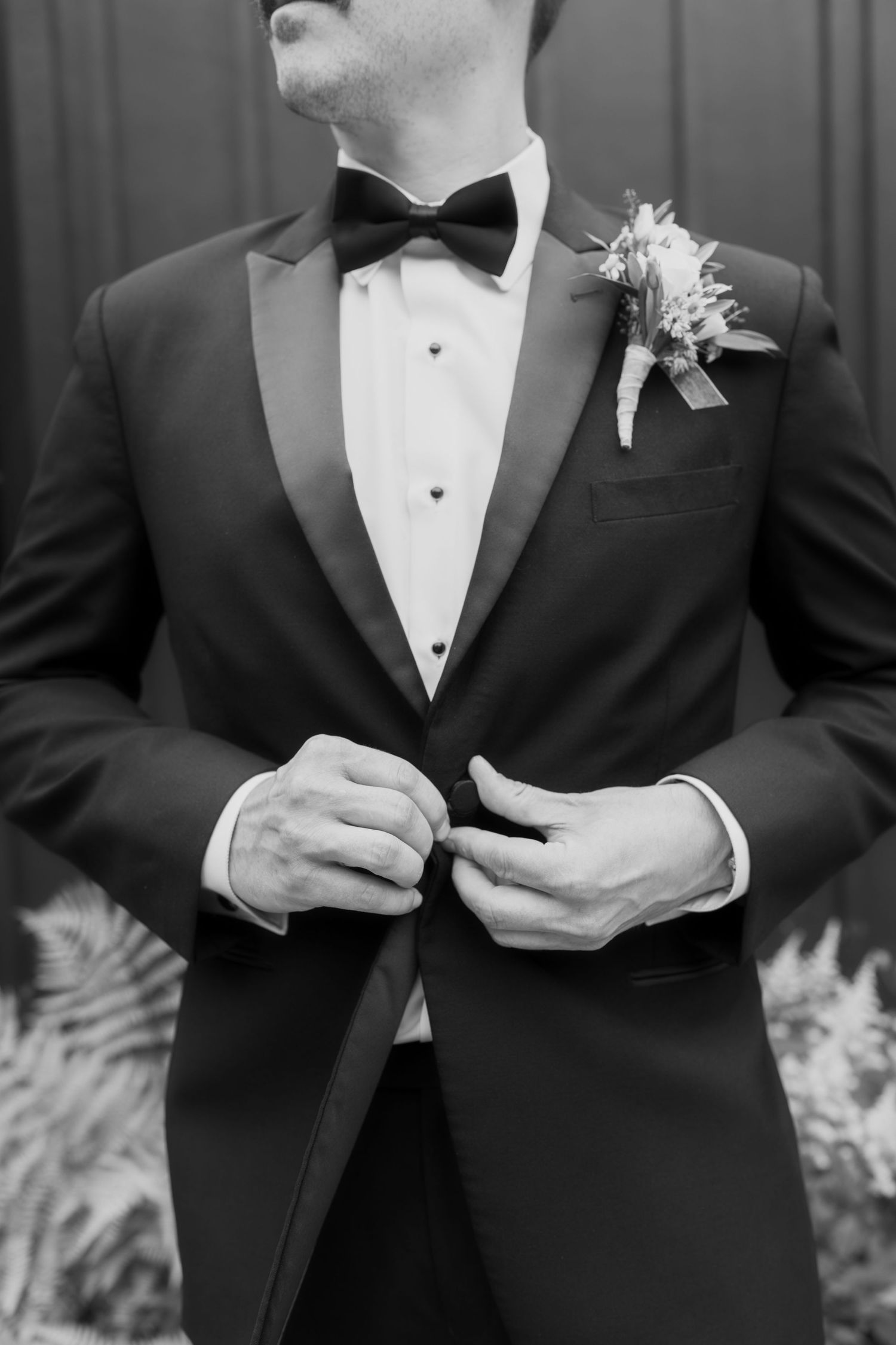 Black and white detail shot of groom adjusting tuxedo jacket and bowtie.