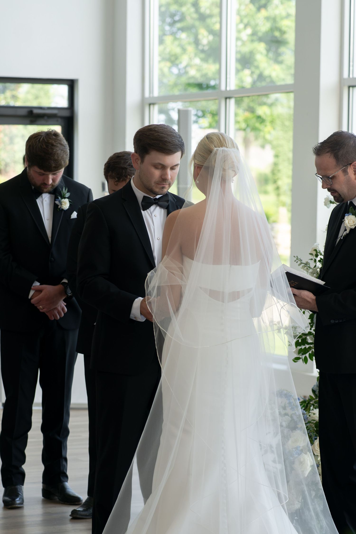 Bride and groom exchange vows at elegant indoor wedding ceremony with groomsmen and officiant nearby.