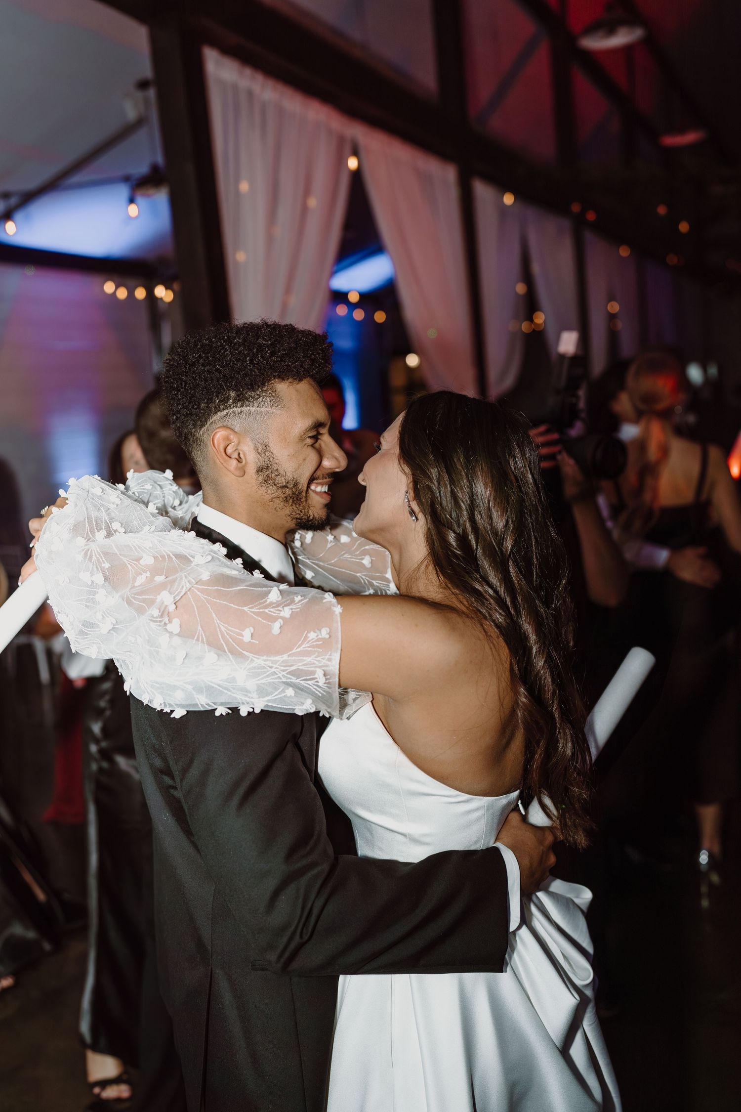 A couple embraces during their first dance at a dimly lit wedding reception.