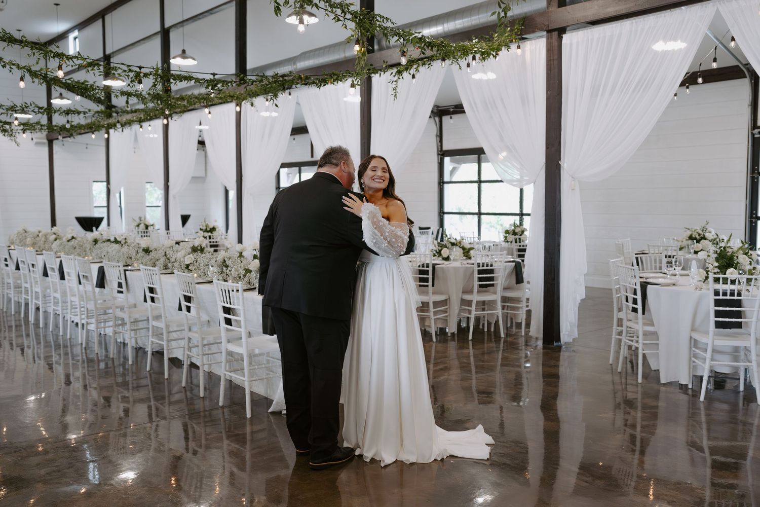 A tender embrace captured in a modern wedding venue with white chairs and draped fabric decor.
