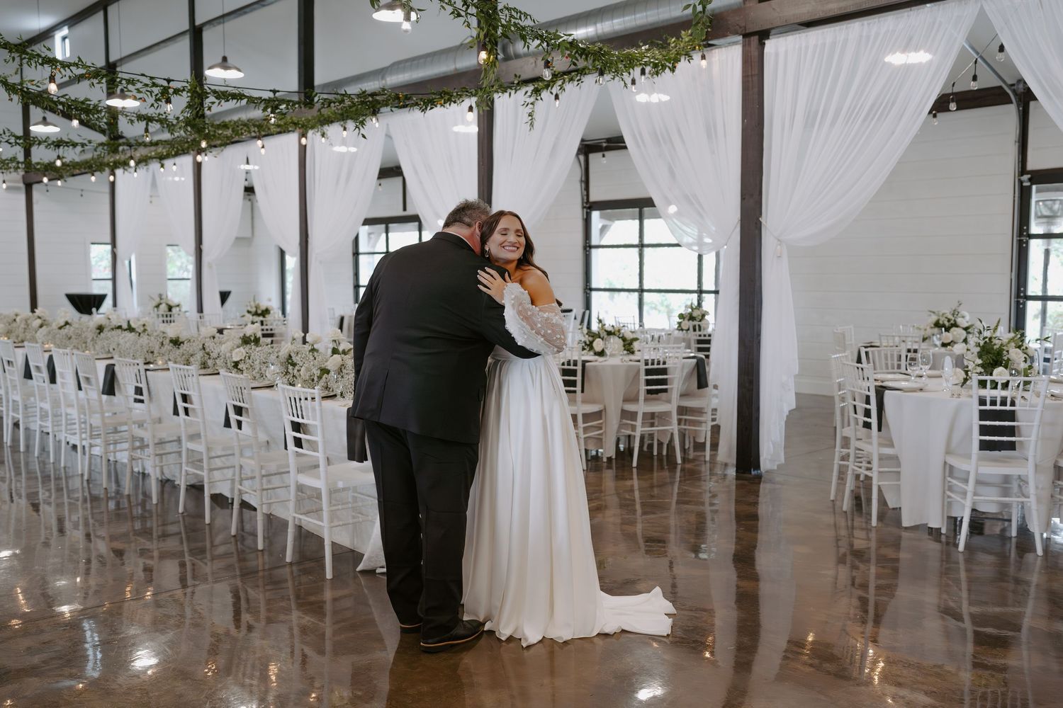 A sweet embrace in a modern wedding venue decorated with white drapes and greenery.