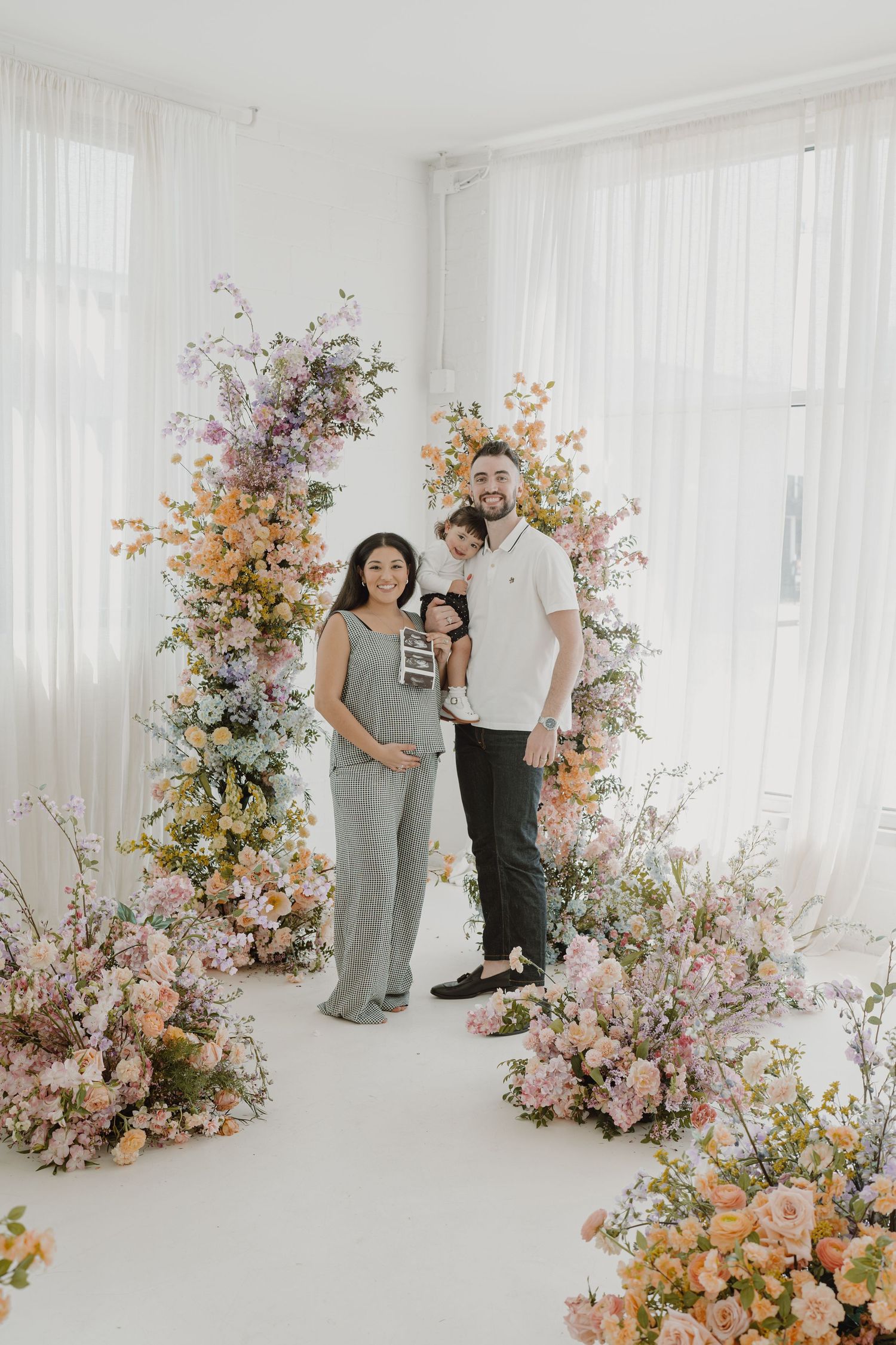 Family photoshoot in a studio decorated with lush pink and peach floral arrangements.