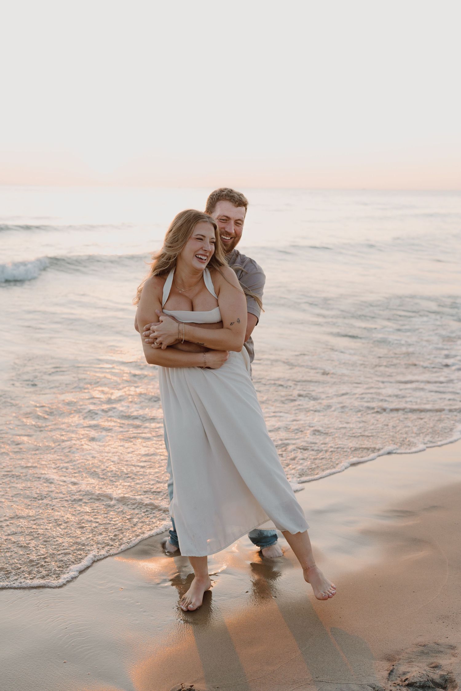 A couple shares a tender moment on the beach as sunset casts golden light on the waves.