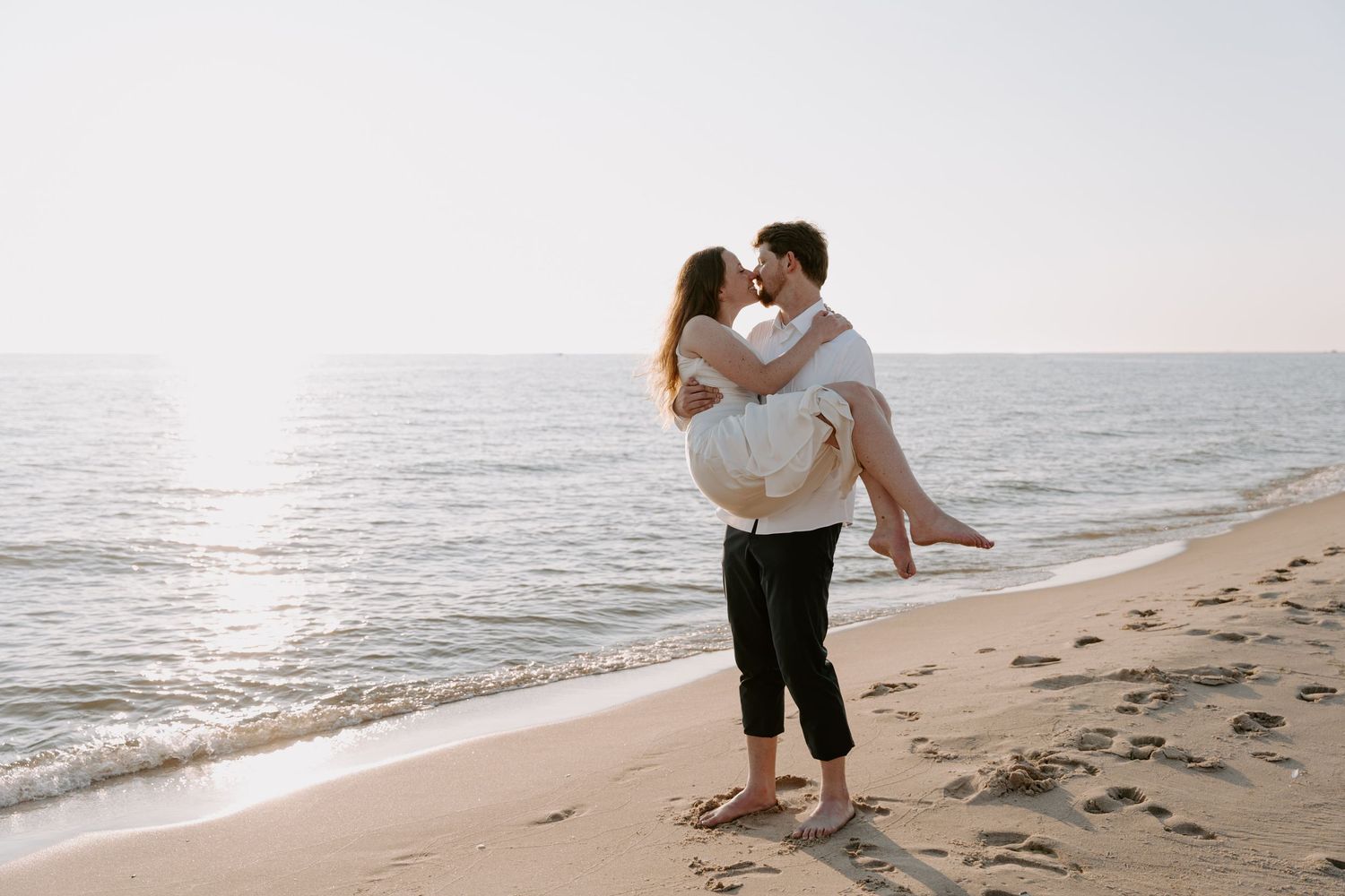 Playful couple moment captured during beach photoshoot with ocean waves.