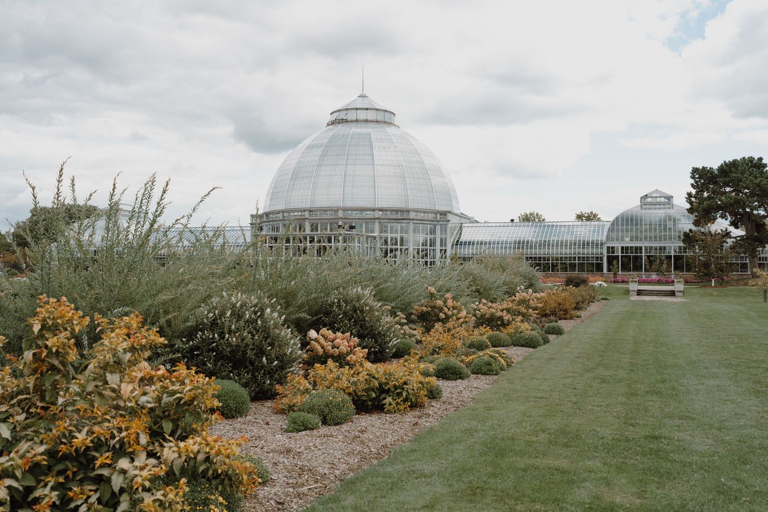 Panoramic view of flowering gardens surrounding a glass domed conservatory.