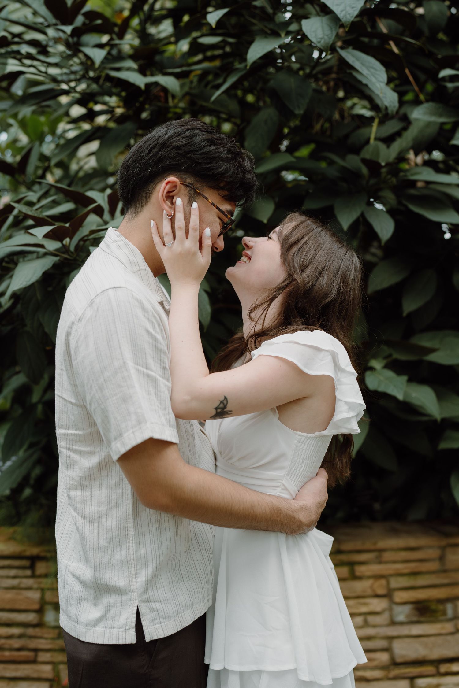 Tender moments between a couple dressed in white against green foliage.