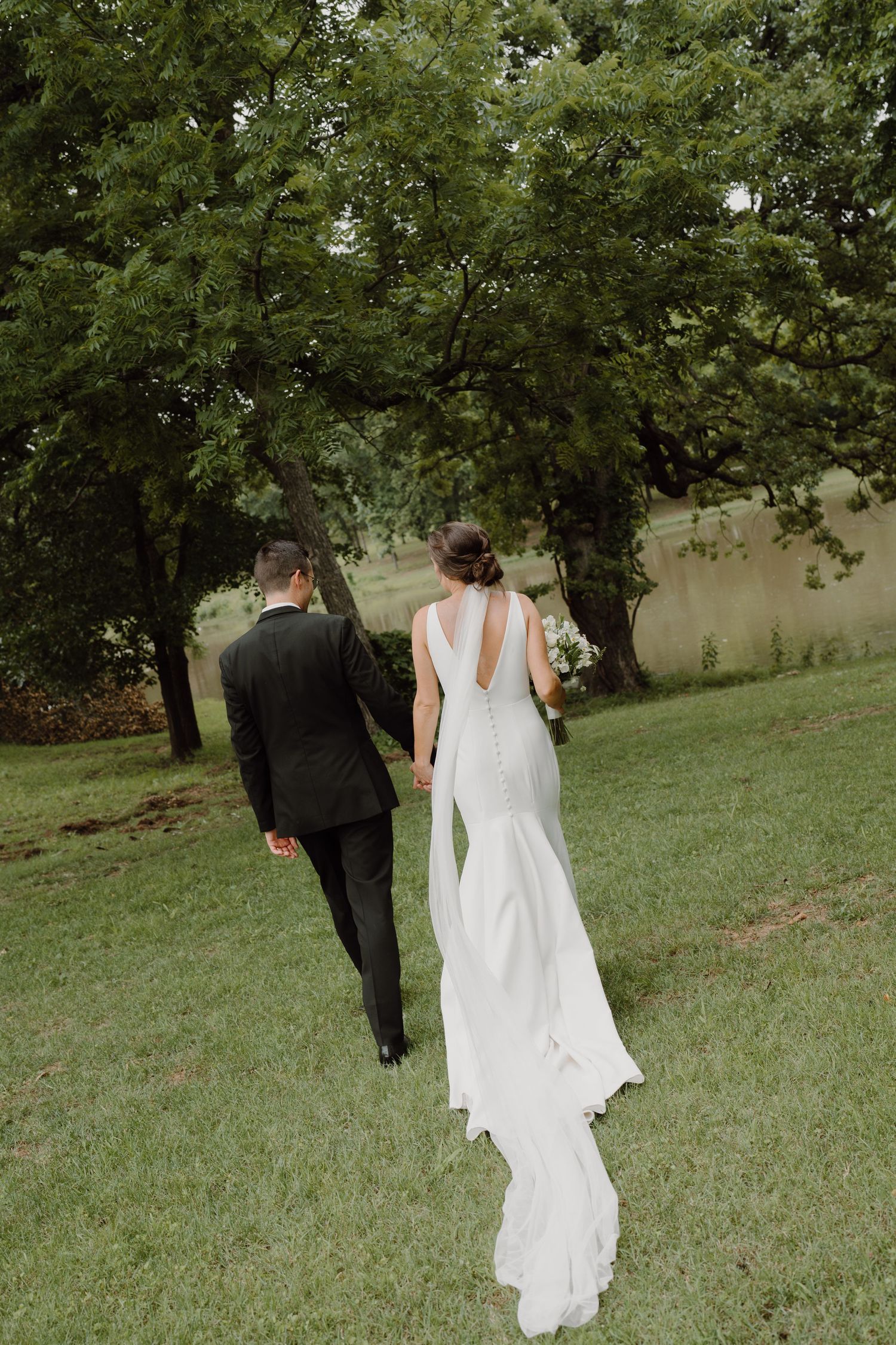 Wedding couple strolling through a scenic park with lush green trees and natural landscaping.