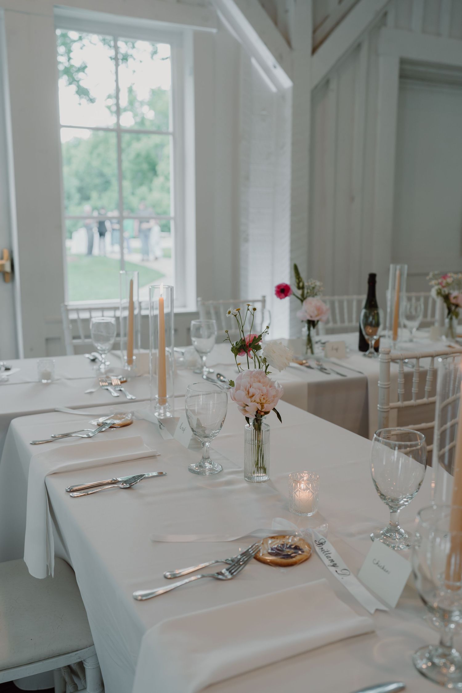 Sunlit wedding reception venue with white decor and elegant table settings.