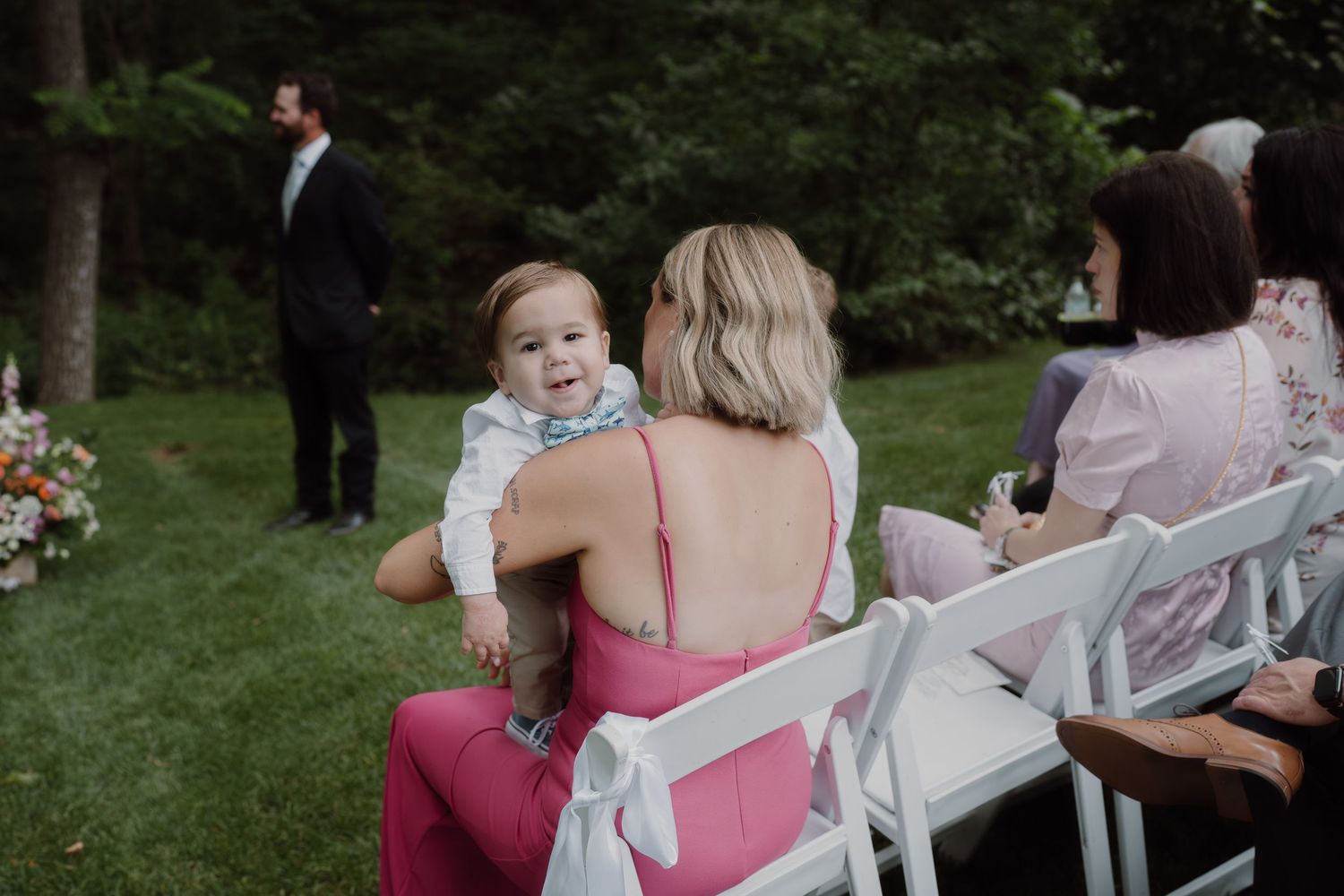 Wedding guests seated in white chairs watching outdoor ceremony.