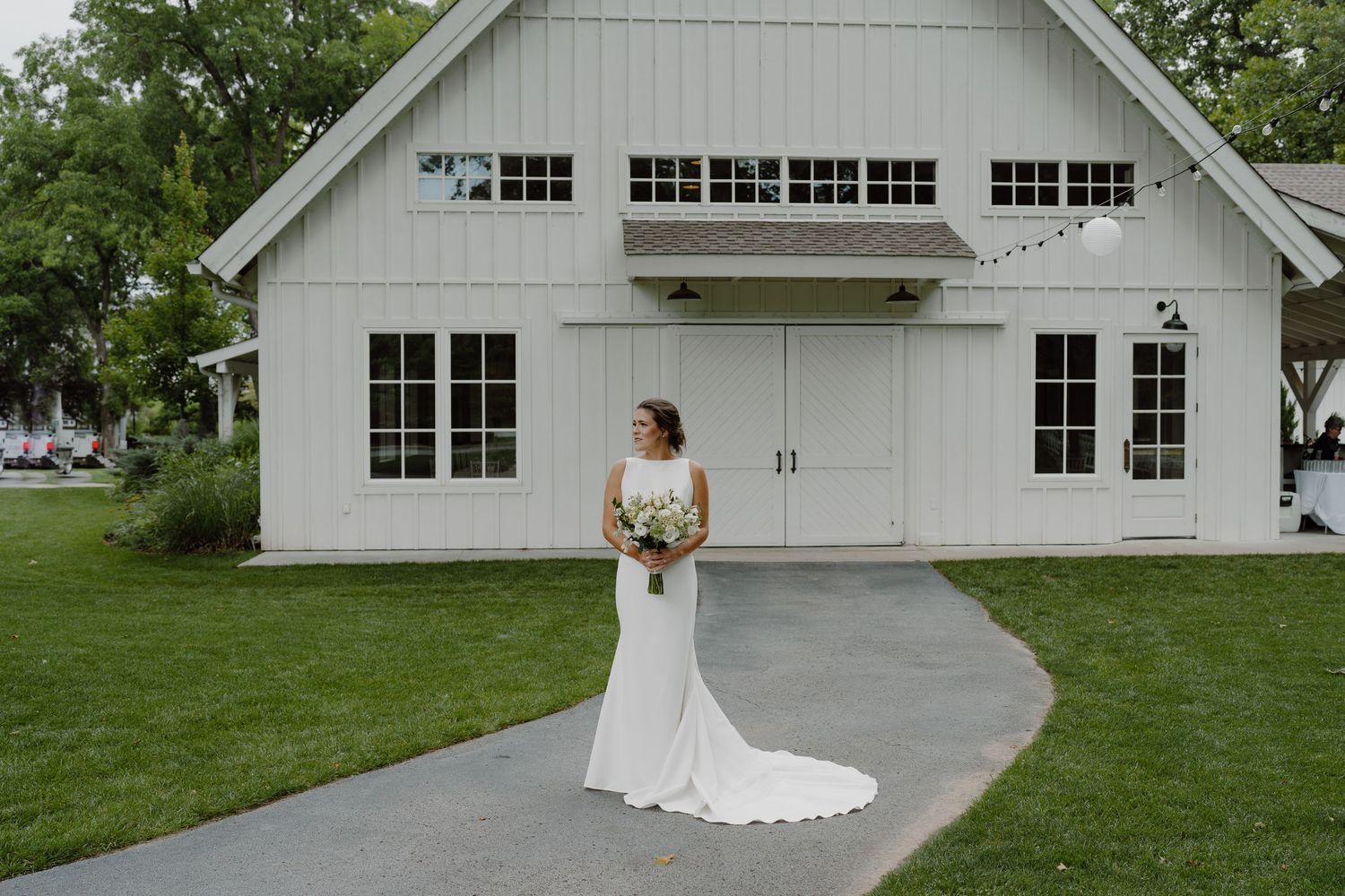 White wedding barn with classic garage doors and lush green landscaping provides an elegant rustic backdrop.