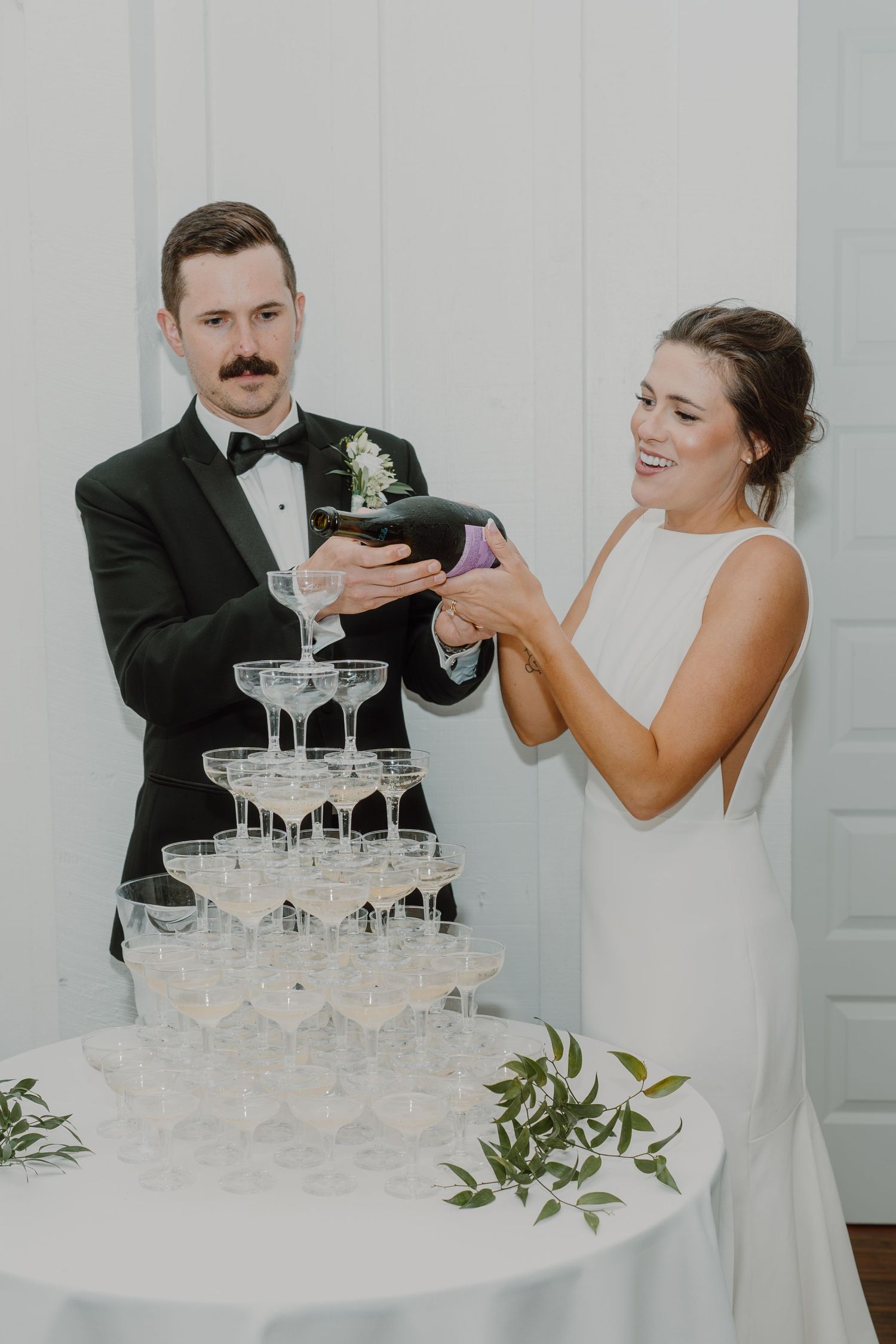 Wedding couple pouring champagne into a tower of elegant crystal glasses.