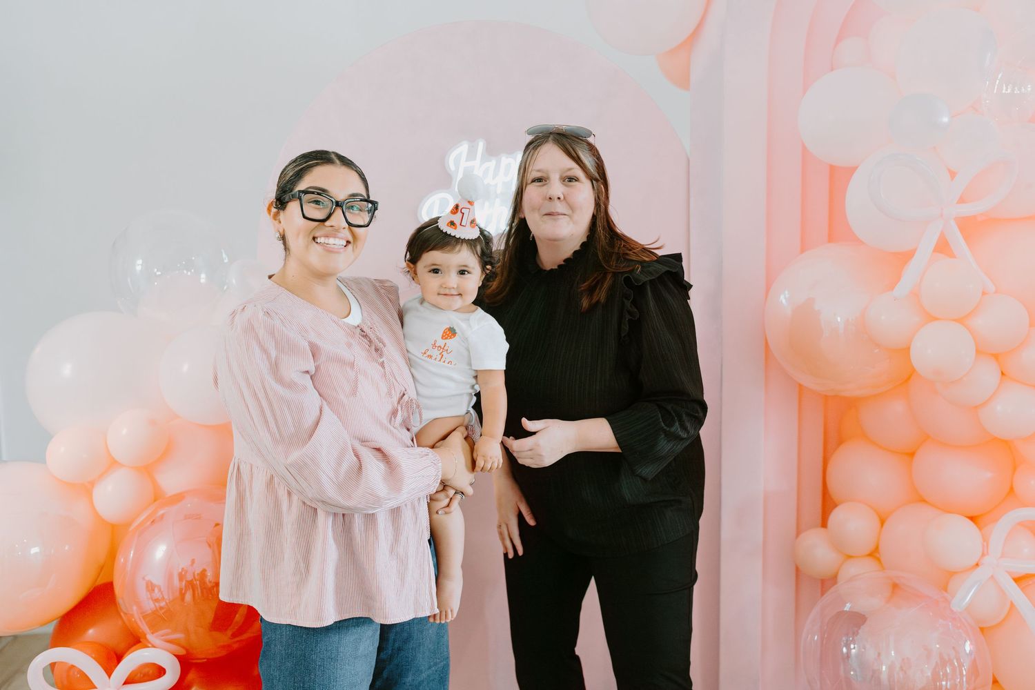 Candid family moments captured in a bright studio with pink balloon decorations.