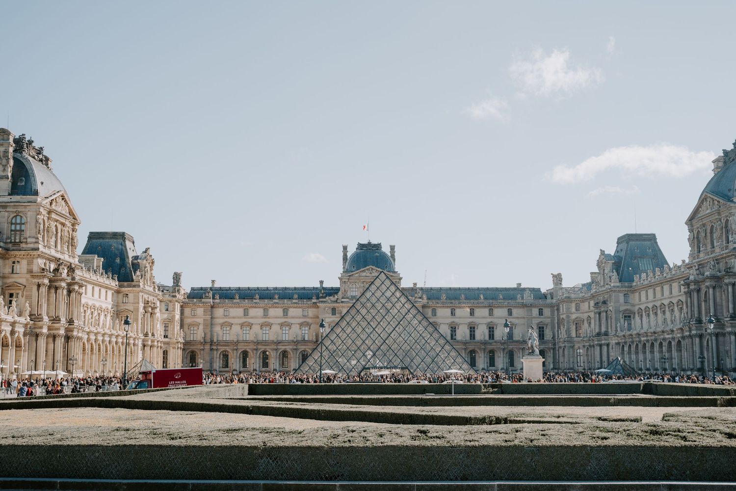 The iconic glass pyramid and historic architecture of the Louvre Museum in Paris on a clear day.
