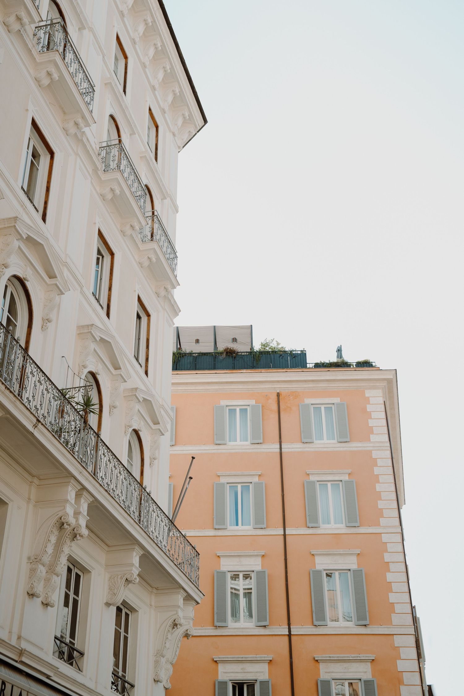 Elegant European buildings with ornate balconies and pastel pink facade against bright sky.