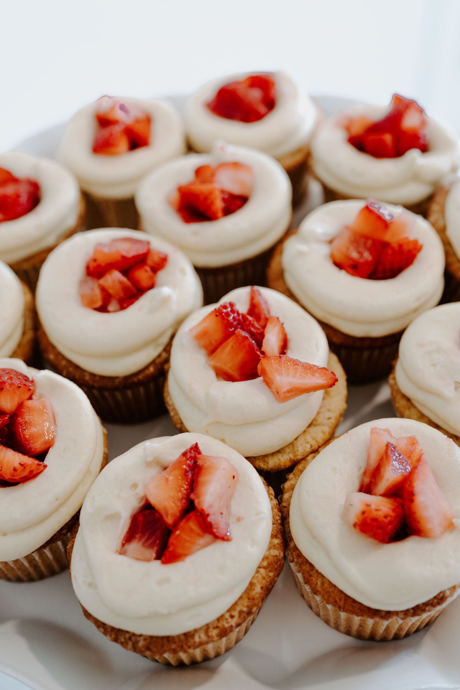Vanilla cupcakes topped with white frosting and fresh diced strawberries arranged on a platter.