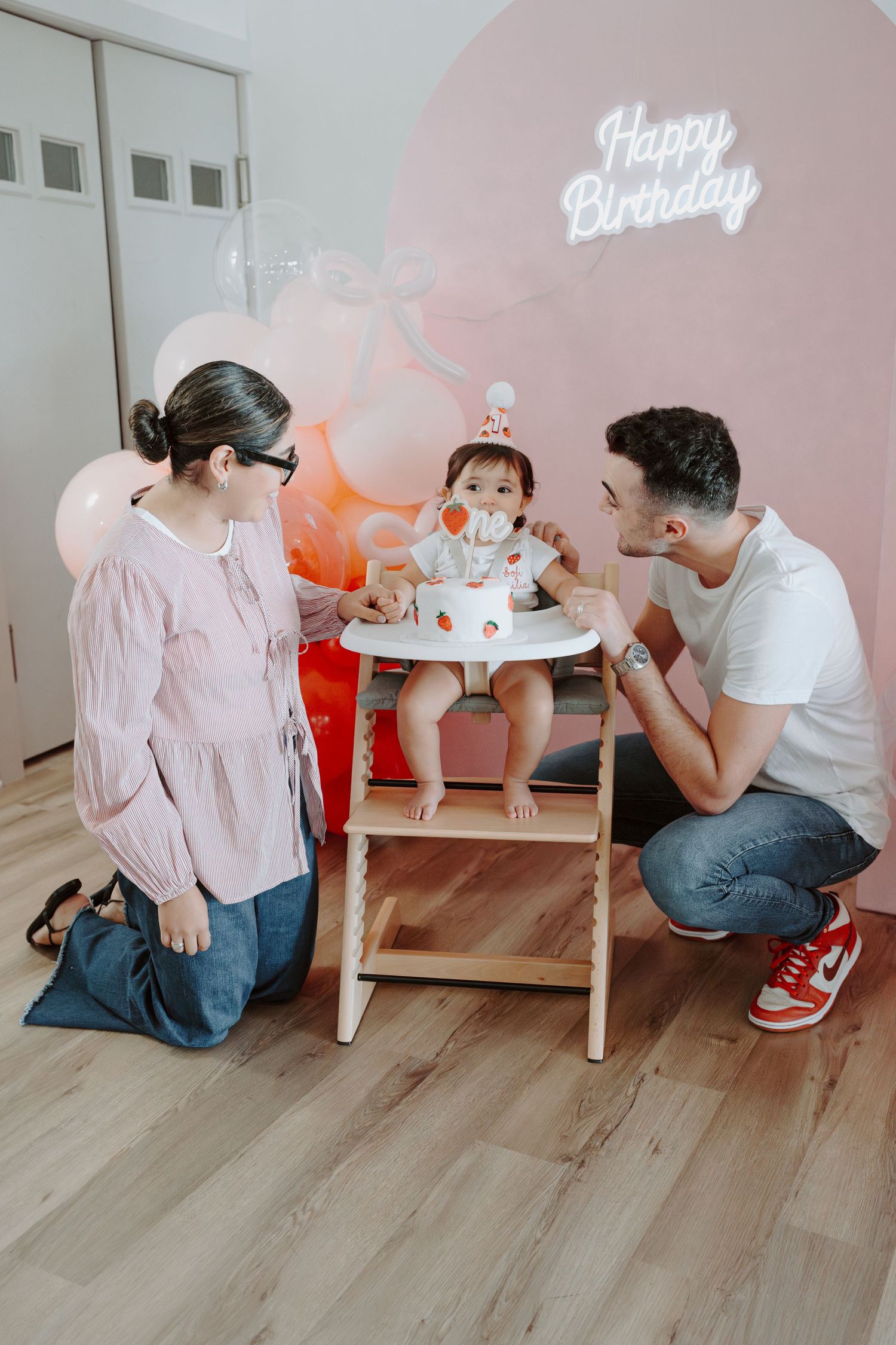 Birthday celebration scene with pink wall backdrop and wooden floor decorations.