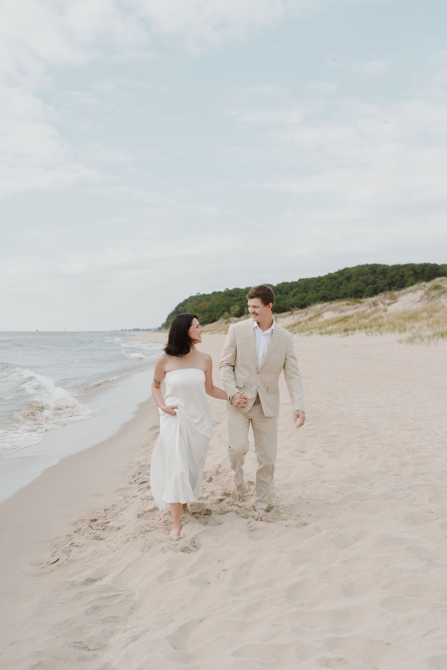 A couple shares a playful moment while walking on a beach near sand dunes.
