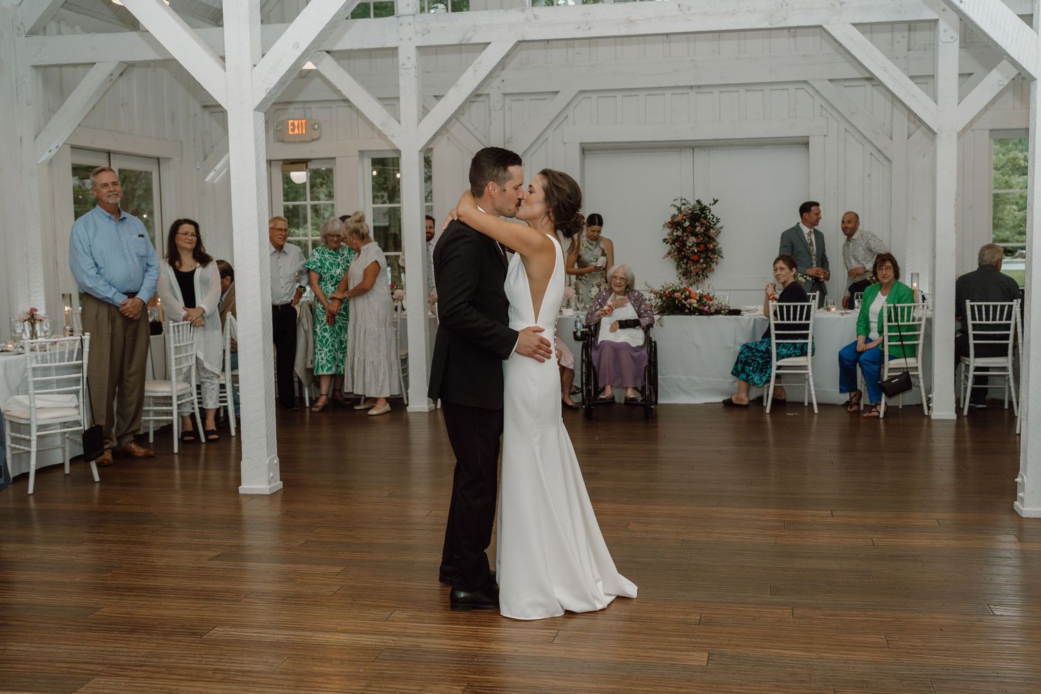 Wedding celebration in a bright white barn venue with couples dancing on hardwood floors.