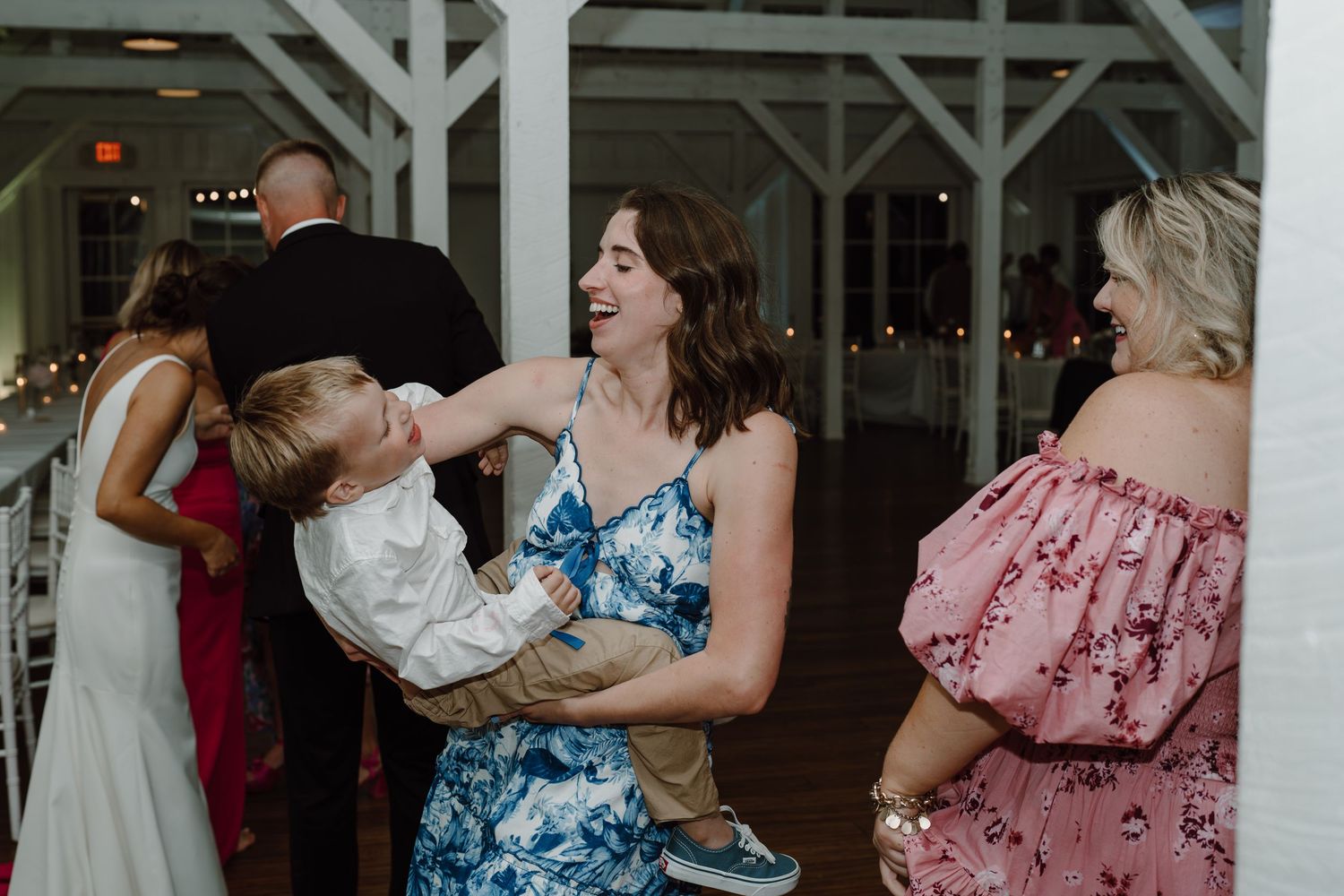 Wedding guests enjoy festivities in a rustic white venue with floral decorations.