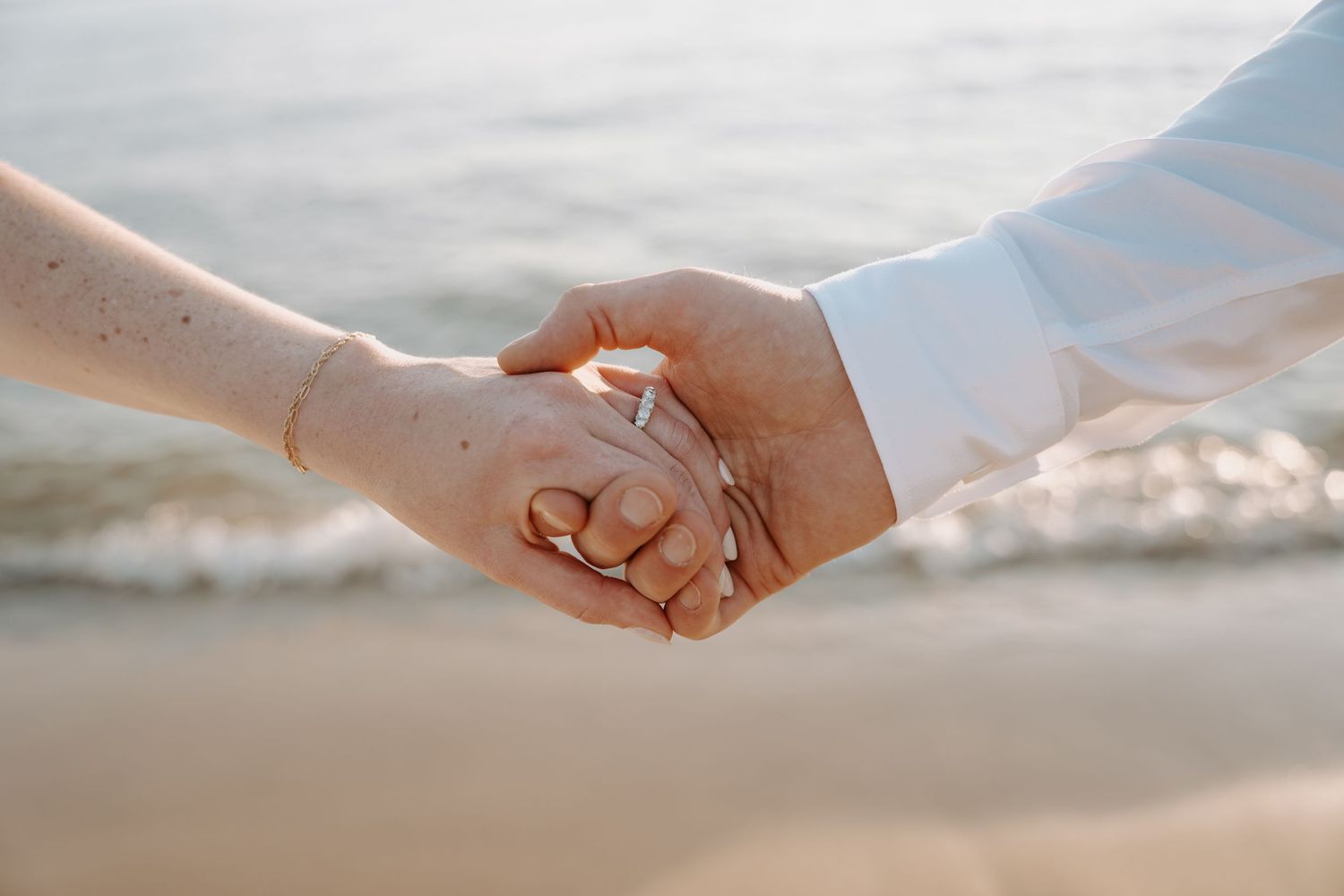 Close-up of hands holding each other against a sunset beach background.