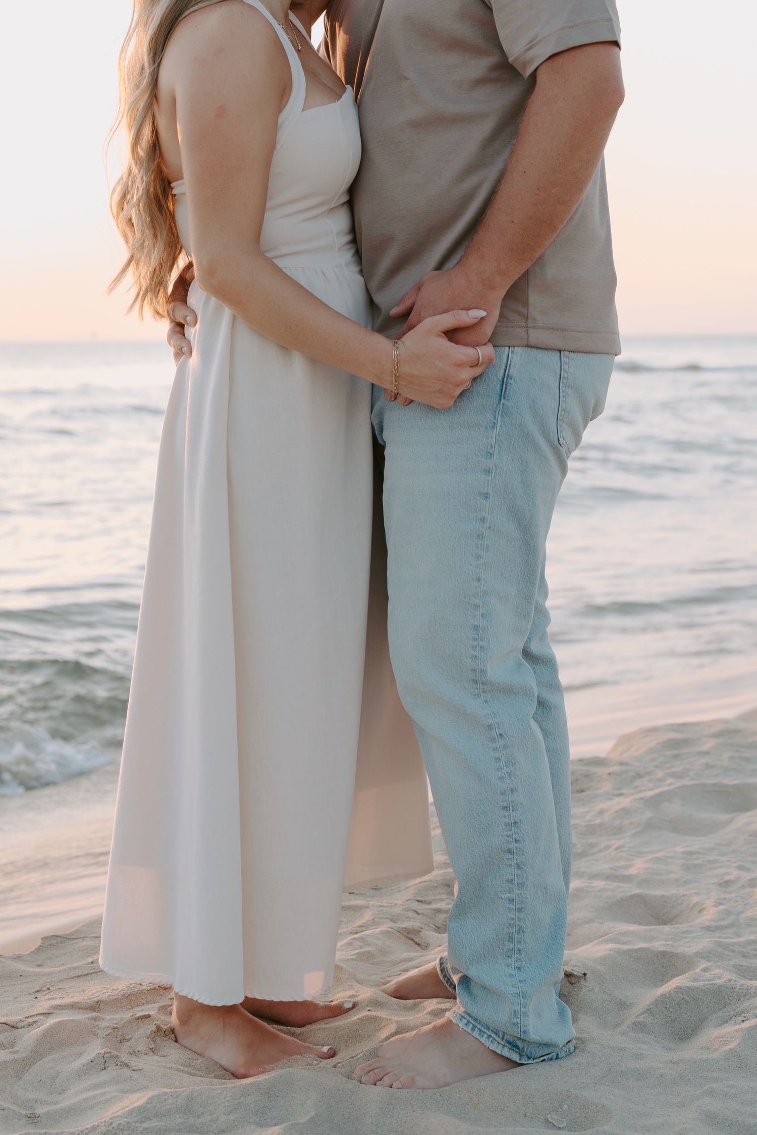Close up of couple holding hands on beach with ocean waves in background.
