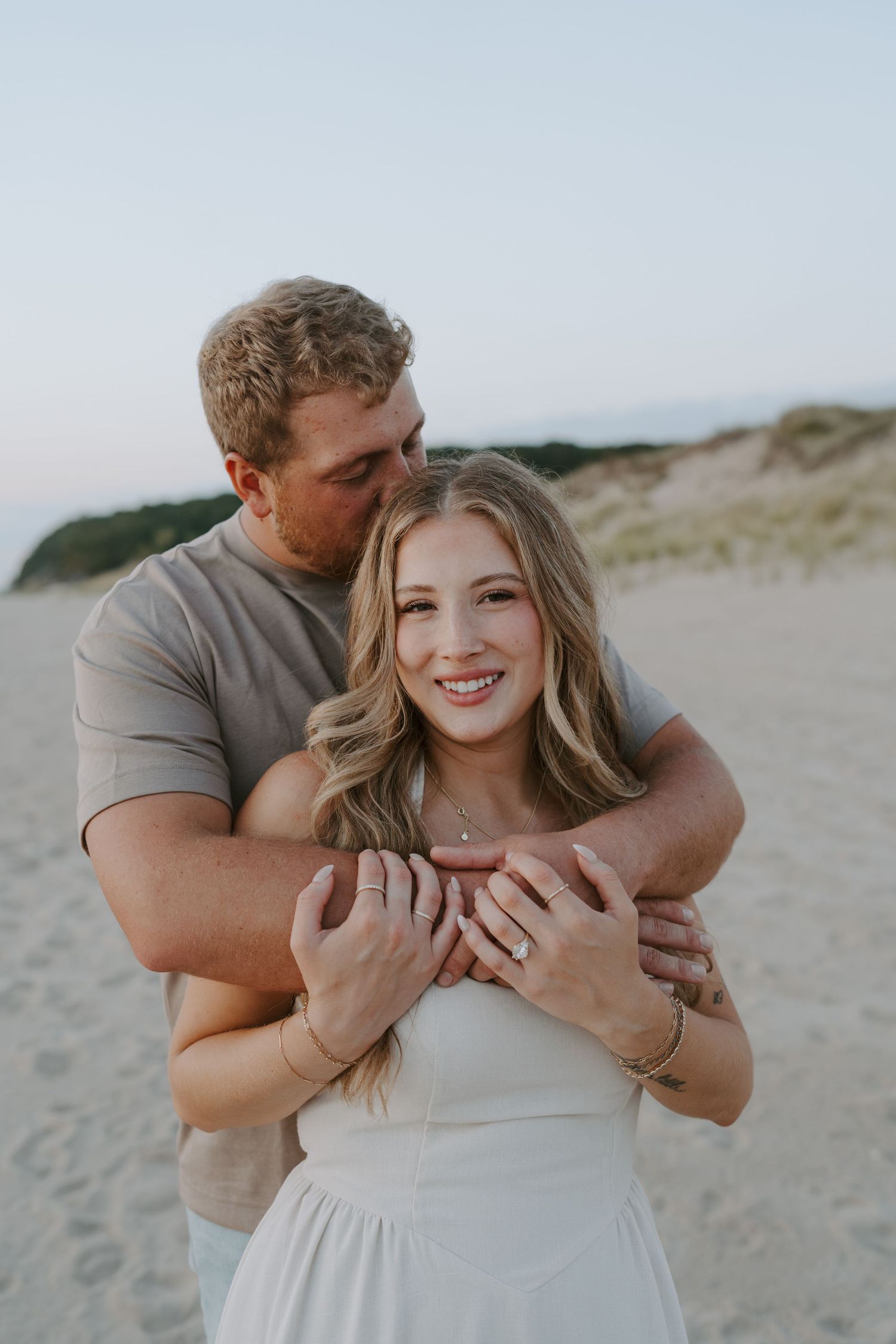 A playful beach engagement session with a couple sharing intimate moments by the dunes.