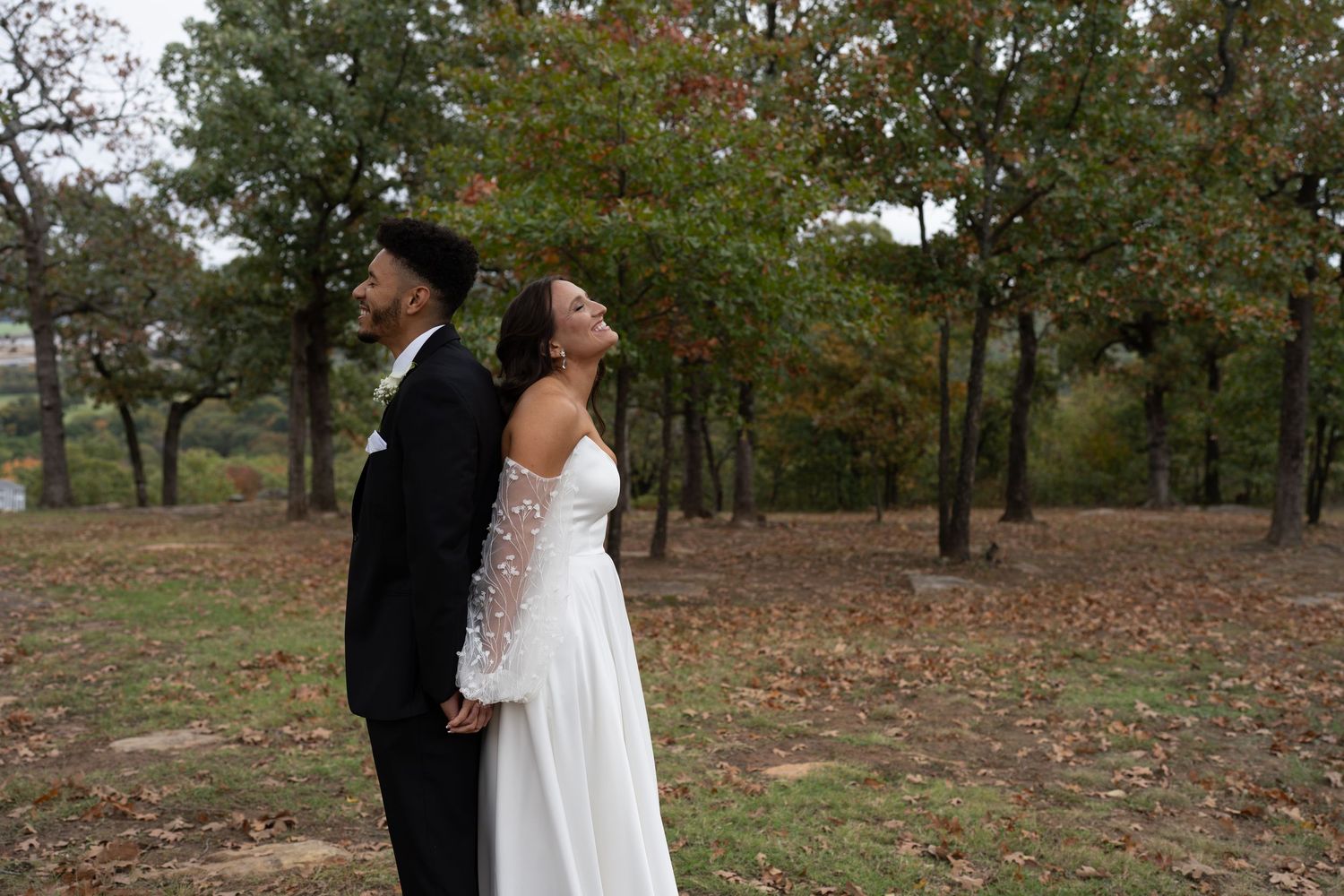 A couple shares an intimate moment outdoors during autumn with fall foliage in the background.