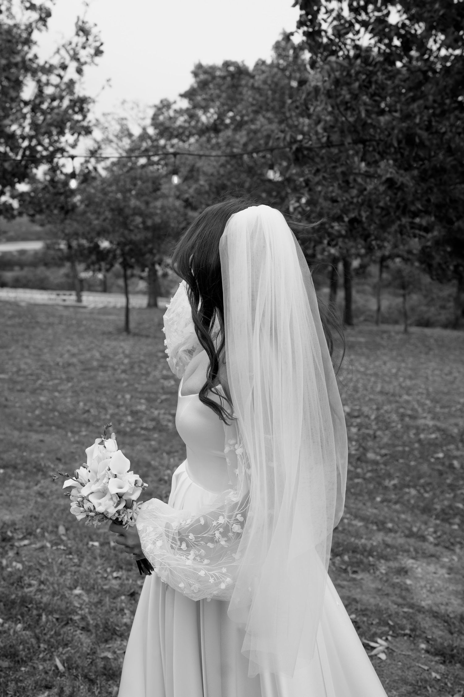 A black and white side profile of a wedding dress with veil and bouquet.