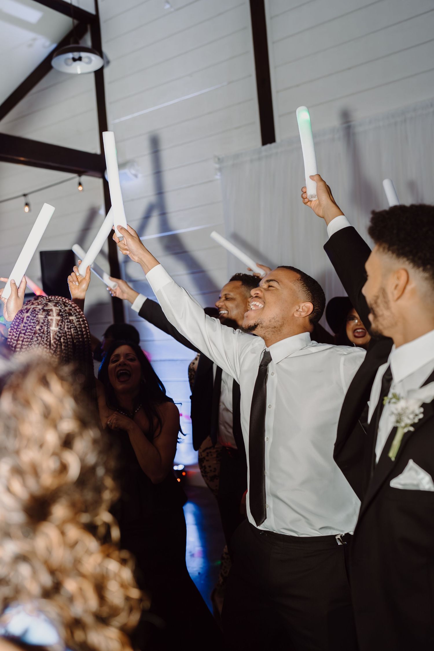 Wedding guests raise illuminated foam sticks in celebration on the dance floor.