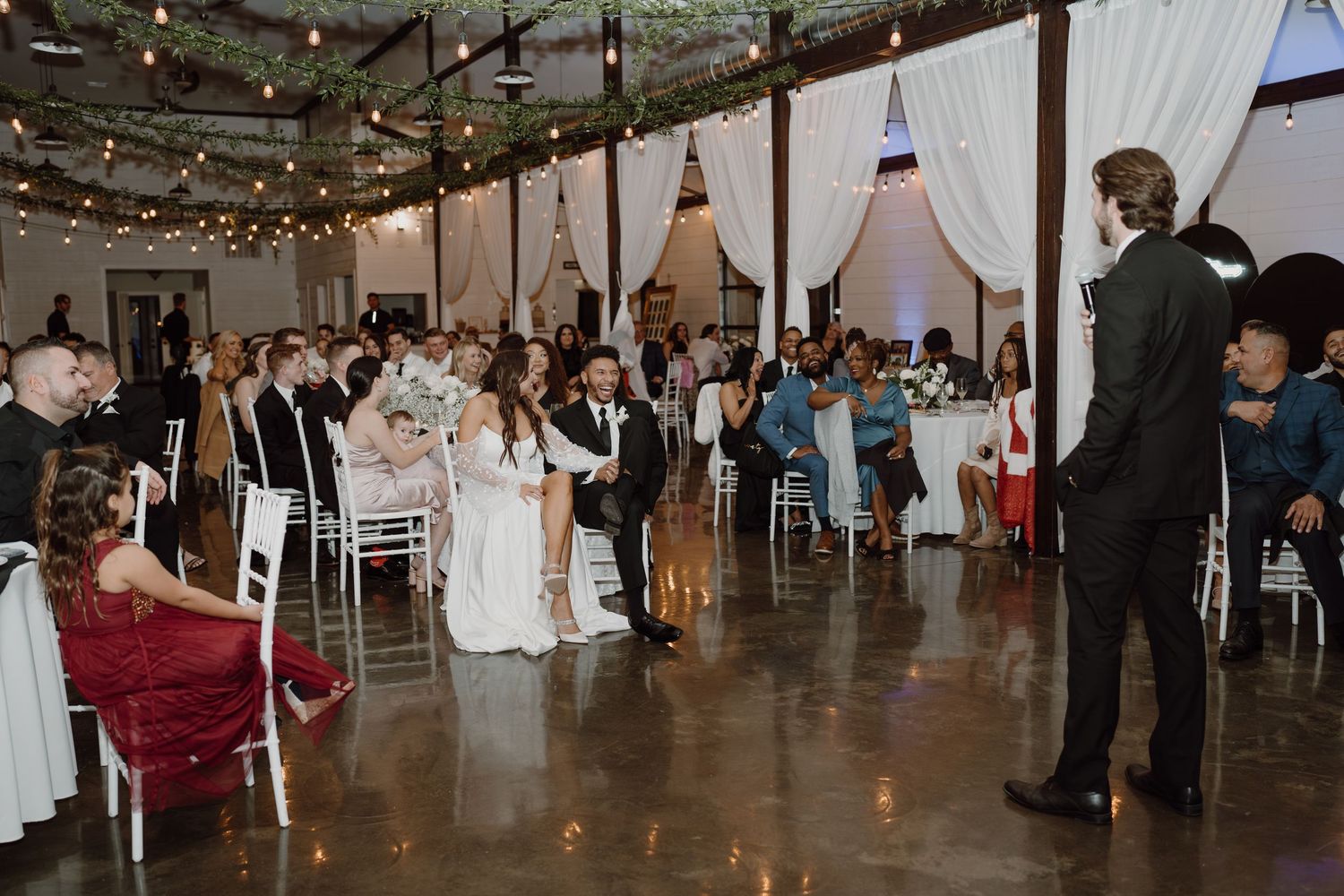 Wedding reception venue decorated with white drapes and string lights during evening celebrations.