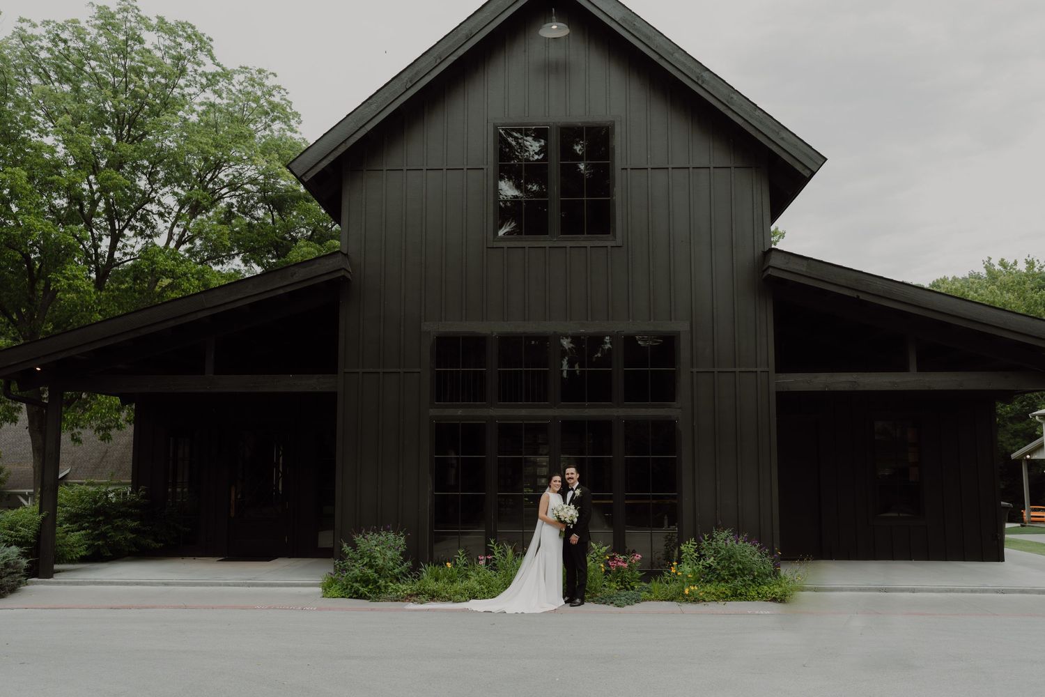 Modern dark gray barn-style building exterior under cloudy skies.